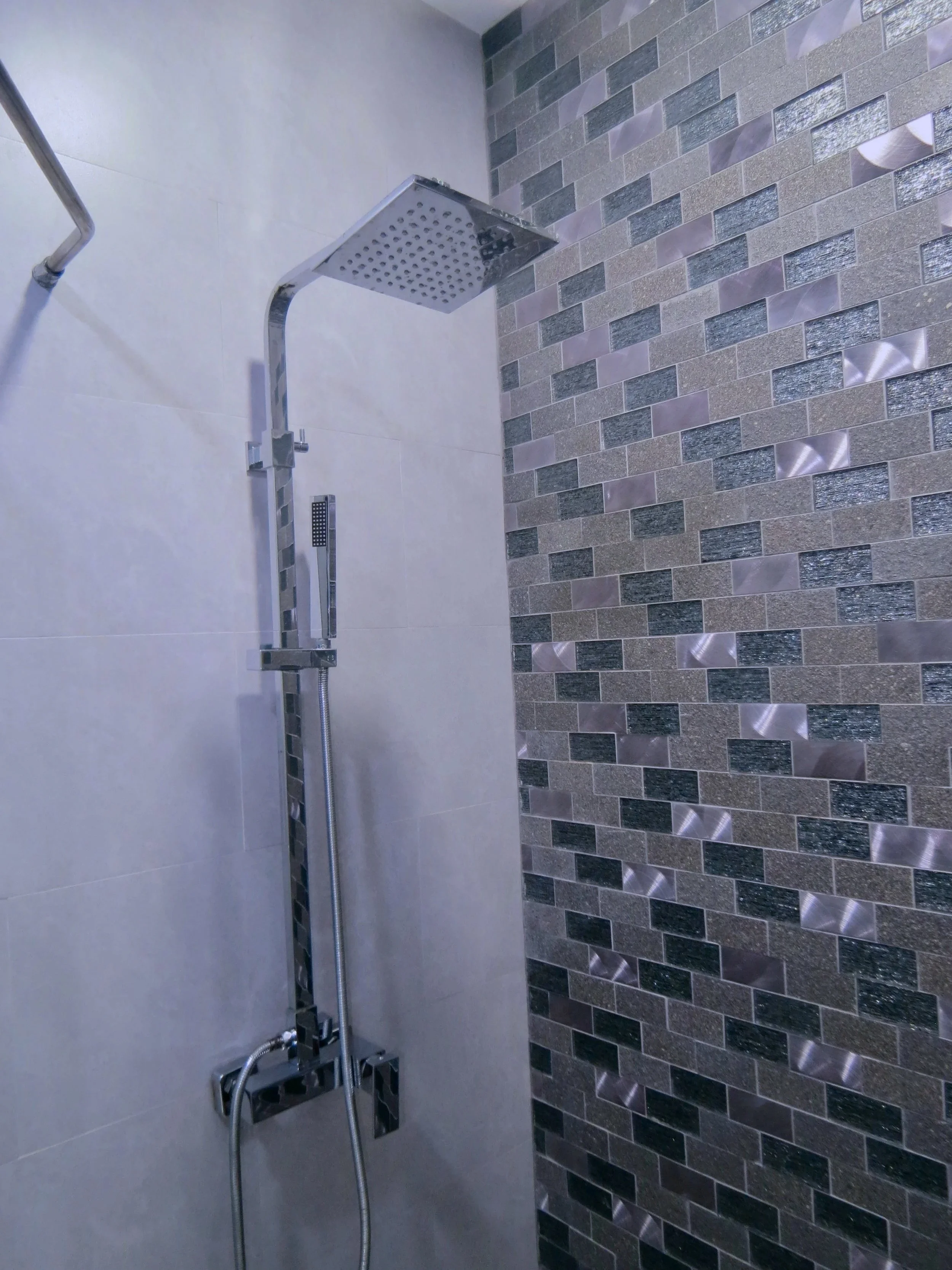 Modern shower with a square rain showerhead and a handheld shower, mounted on a wall with decorative tile accents.  Unit S2, Caye Caulker,  Blu Zen Belize