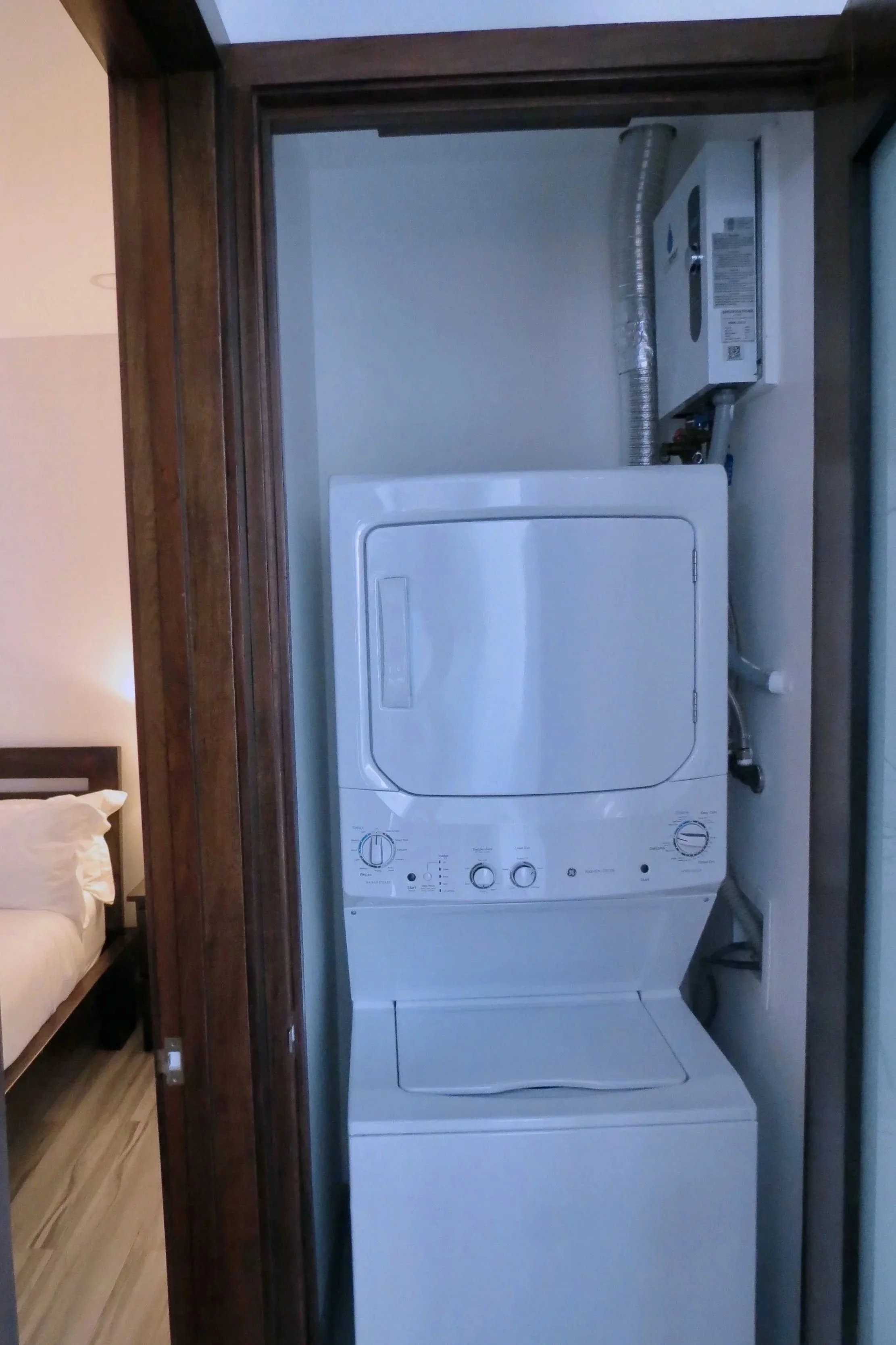 A stacked washer and dryer unit inside a laundry room, with guest bedroom partially visible to the left.  Unit S2, Caye Caulker,  Blu Zen Belize