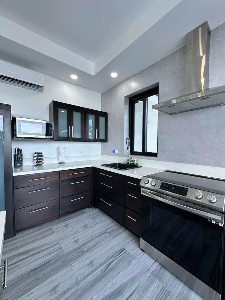 Modern kitchen with dark wood cabinets, white countertops, a window, a stove, microwave, and various kitchen appliances.  Unit S2, Caye Caulker,  Blu Zen Belize