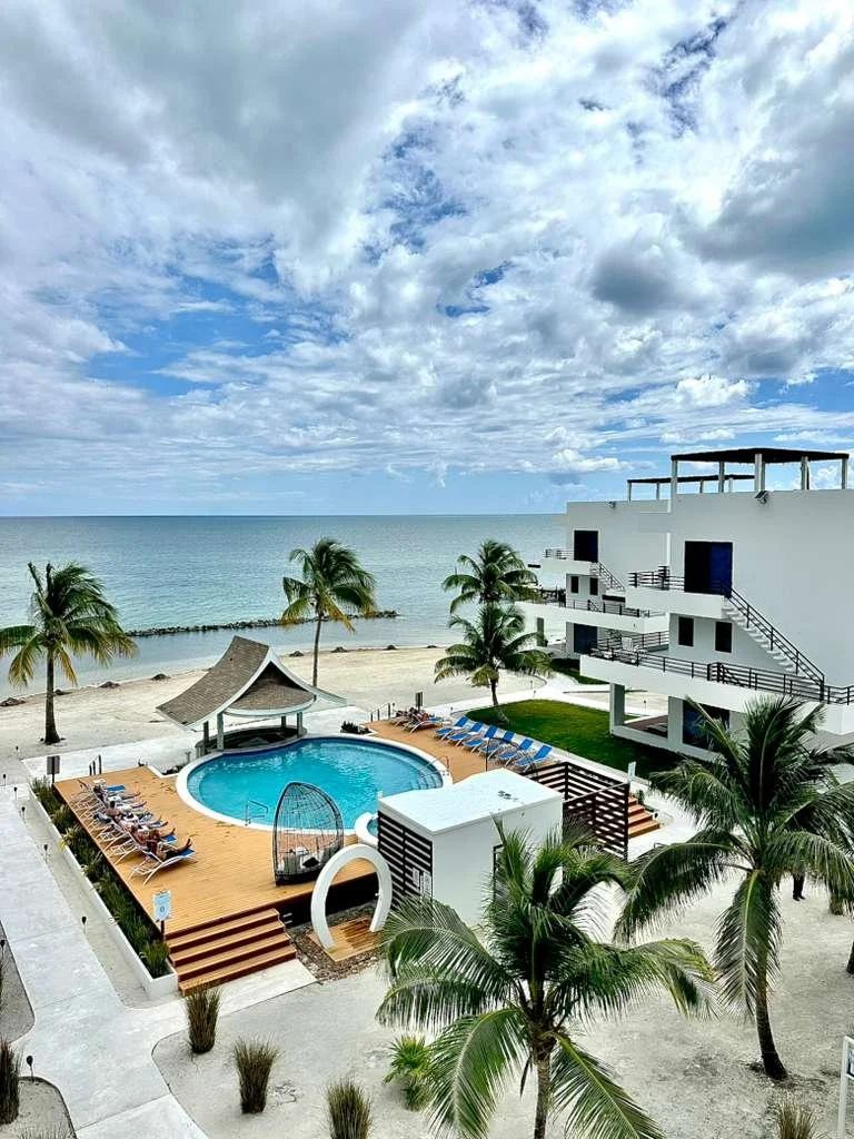 Blu Zen Phase 3 swimming pool, beachside palm trees, and white condo buildings under a cloudy sky. This is 1 of 3 swimming pools.  Unit S2, Caye Caulker,  Blu Zen Belize 