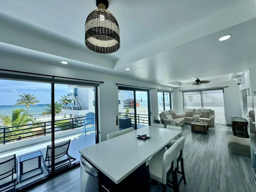 Bright living room with large windows, ocean view, outdoor balcony, beige sofas, and beach scenery.  Unit S2, Caye Caulker,  Blu Zen Belize