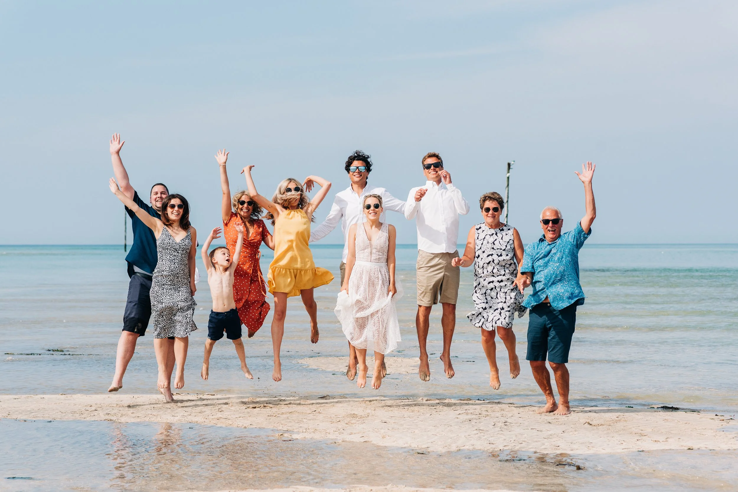 A group of people on a beach jumping in the air and smiling, with the ocean and sky in the background.