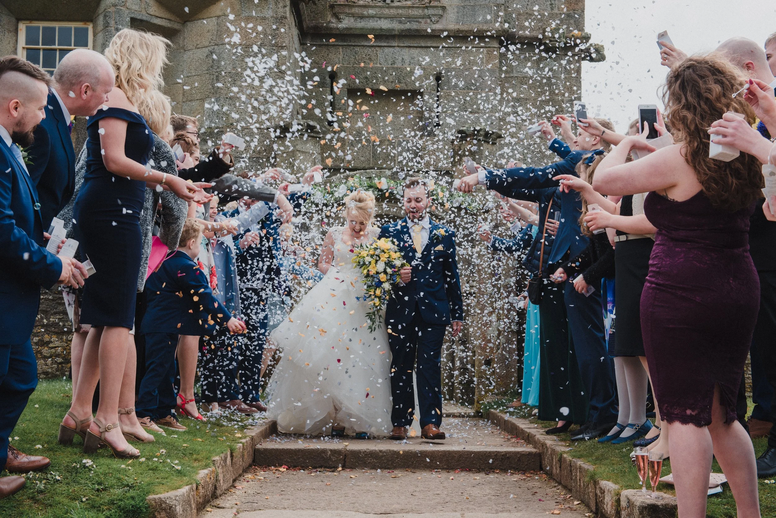 Bride and groom walking out of a church, surrounded by guests throwing confetti.