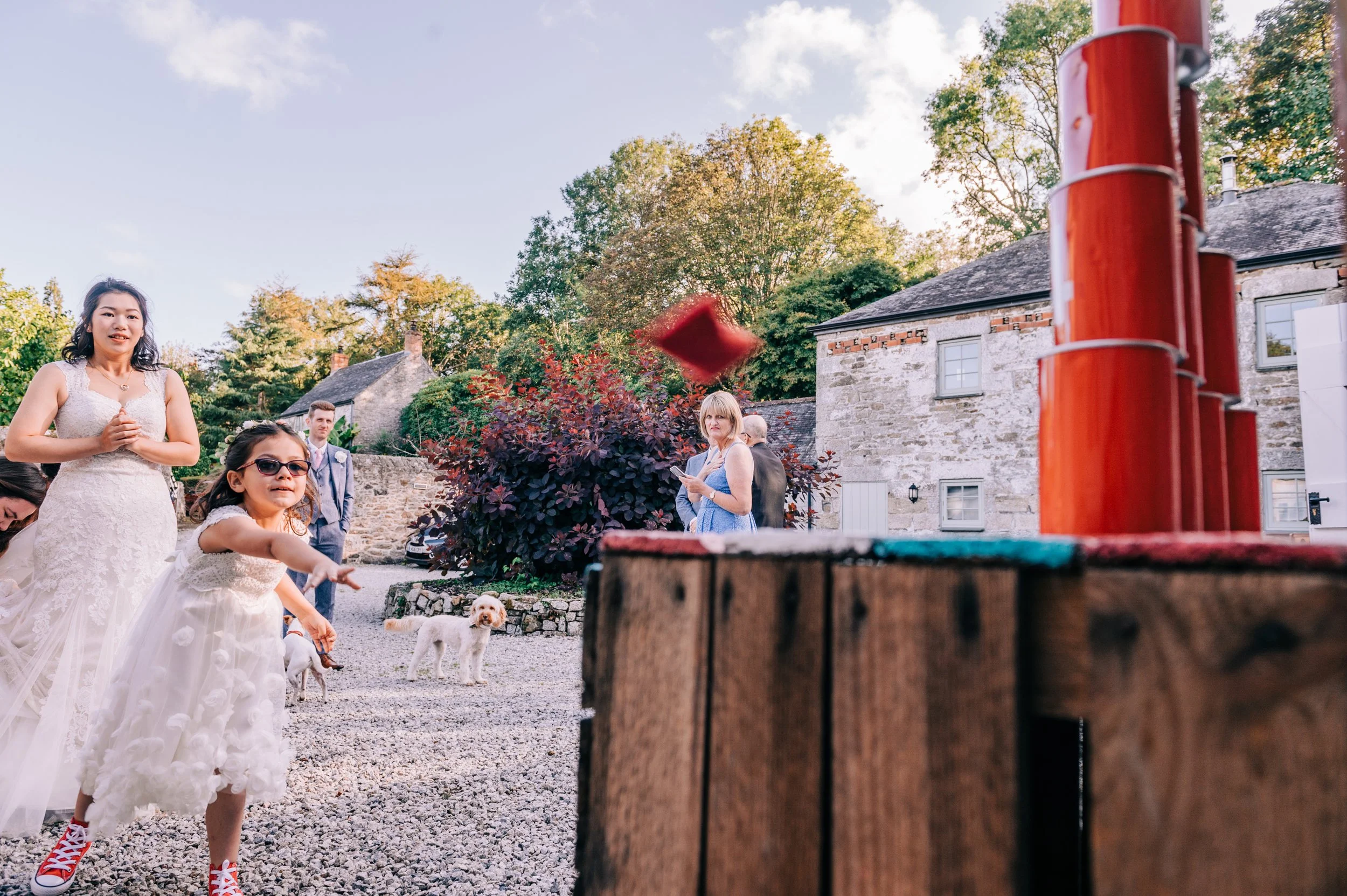 People playing outdoor game at a gathering, with children throwing rings and adults watching, in a rural setting with stone houses and trees.
