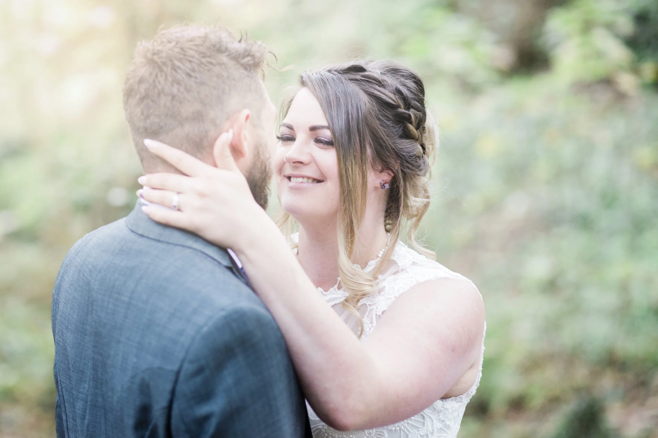 A bride and groom embrace outdoors, smiling at each other during their wedding.