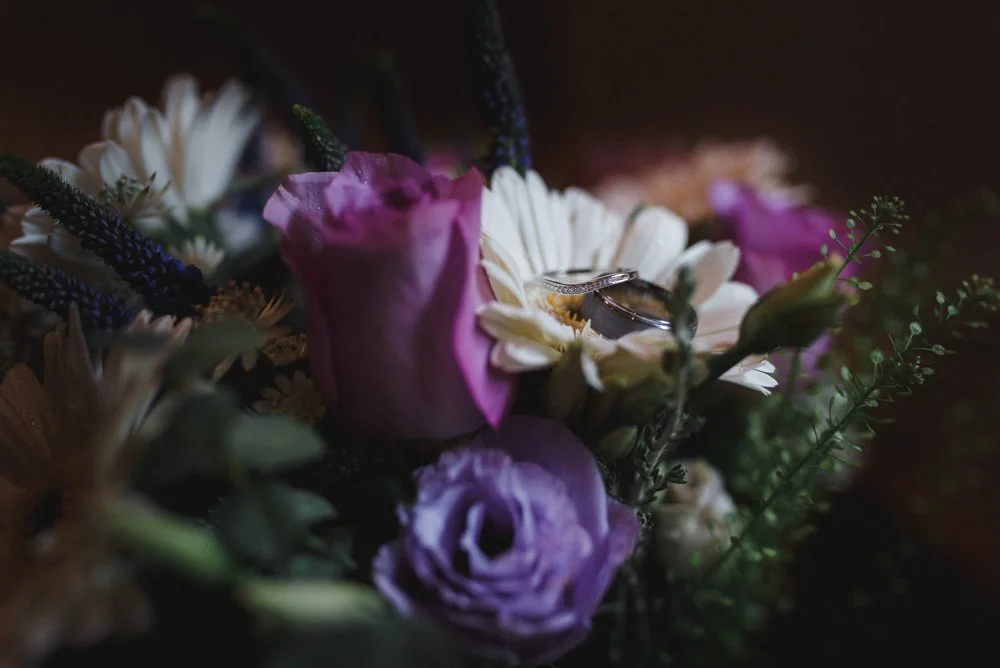 Close-up of a bouquet of mixed flowers with rings placed on a white flower at the center.
