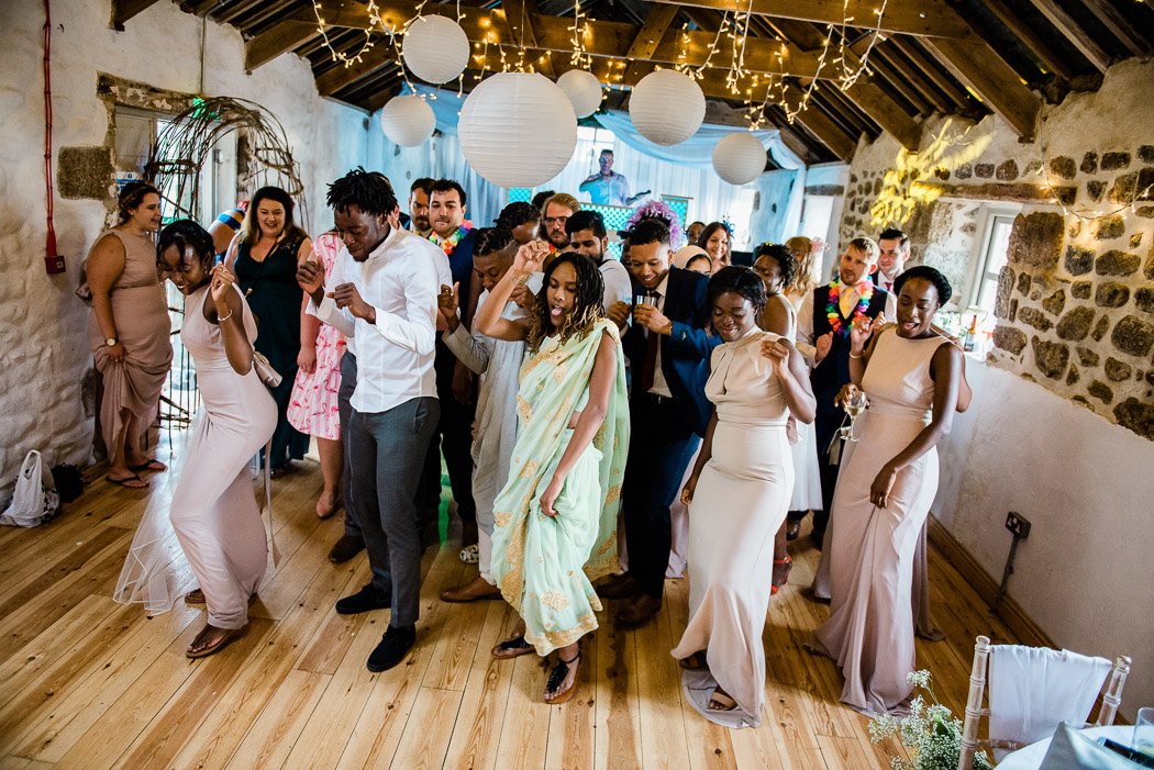 Group of people dancing at a celebration in a rustic hall decorated with paper lanterns and fairy lights.