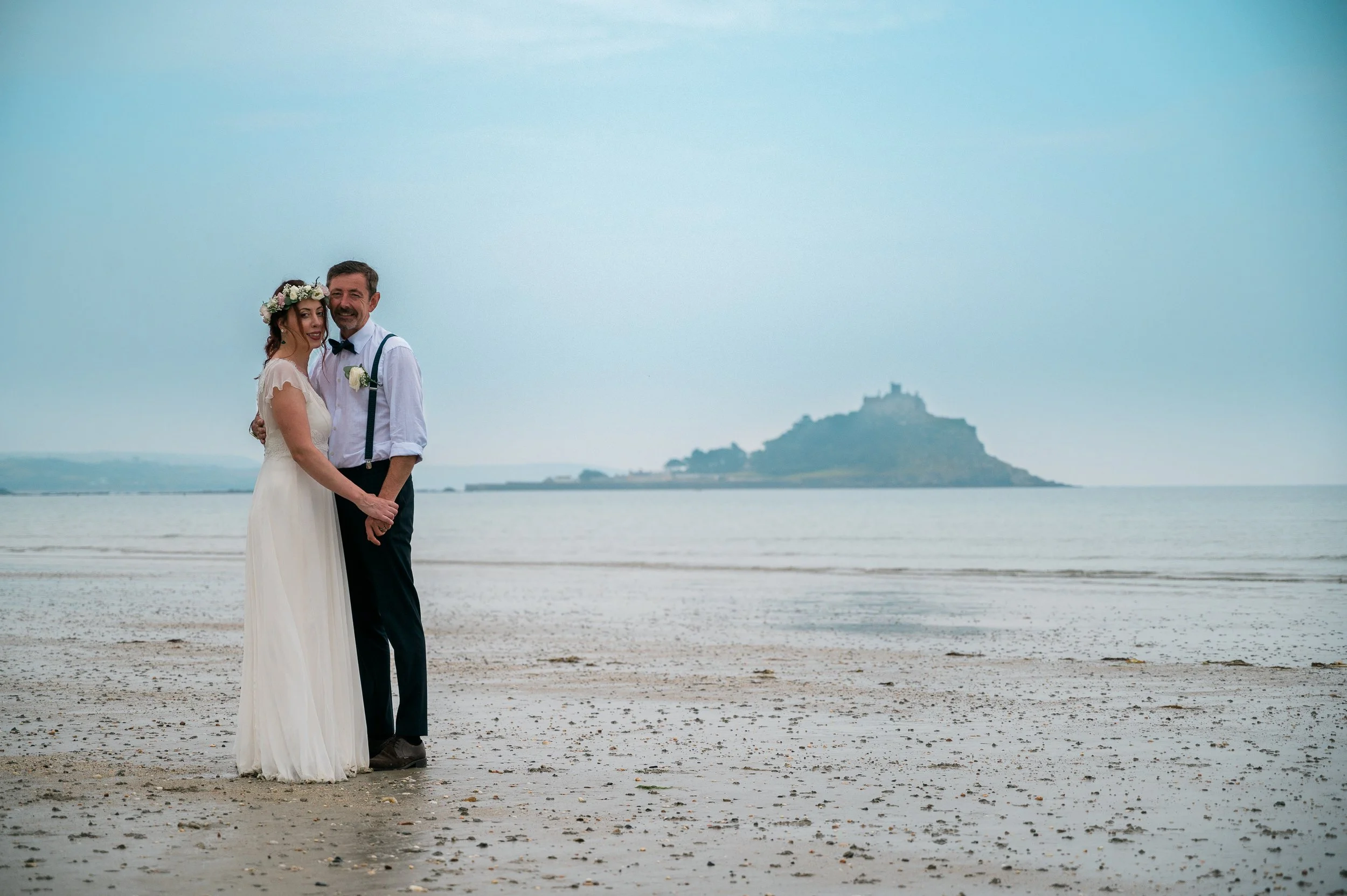 Wedding couple standing on a beach with an island in the background during daytime.