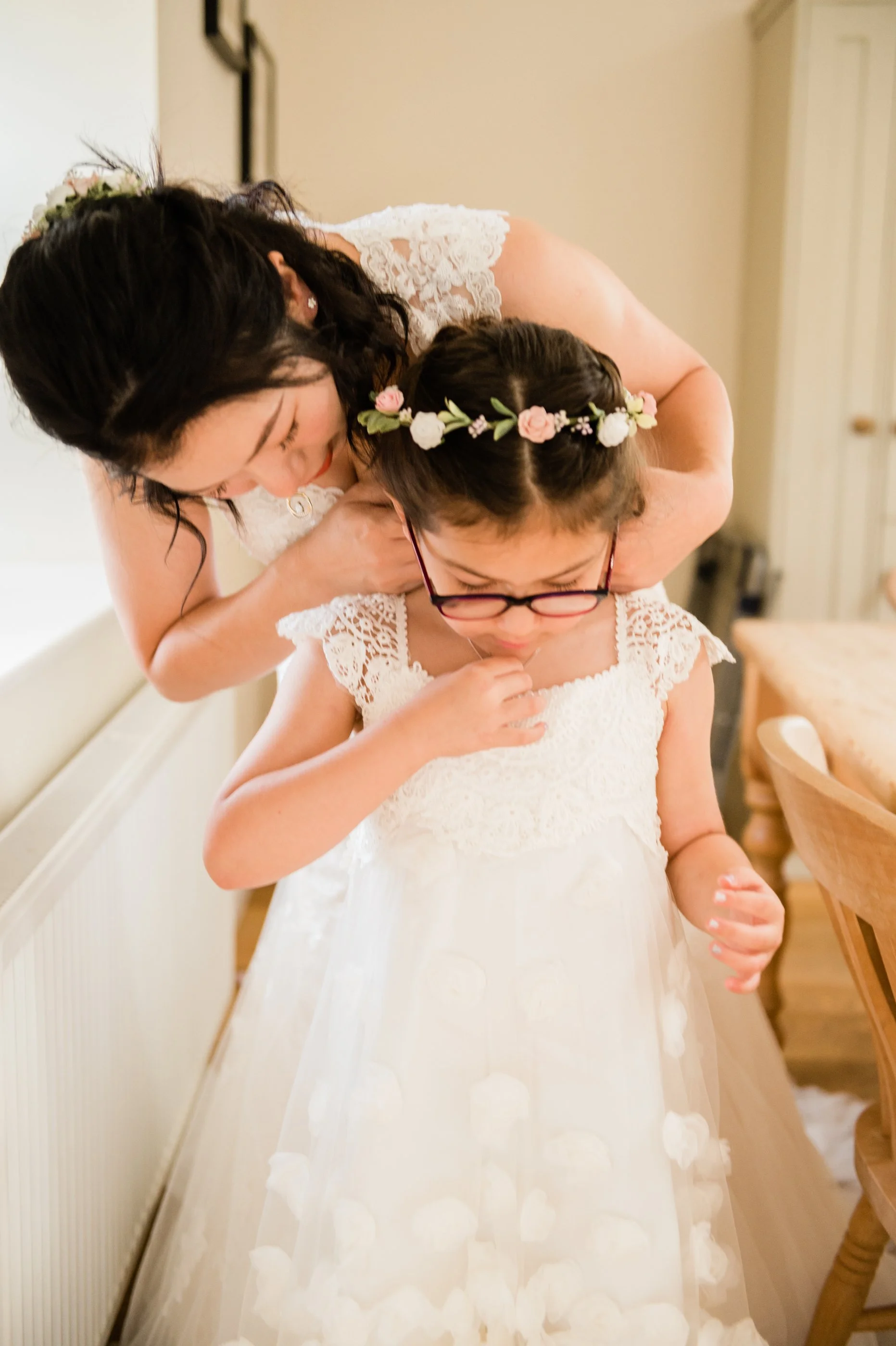 A woman helping a young girl in a white dress and floral crown.