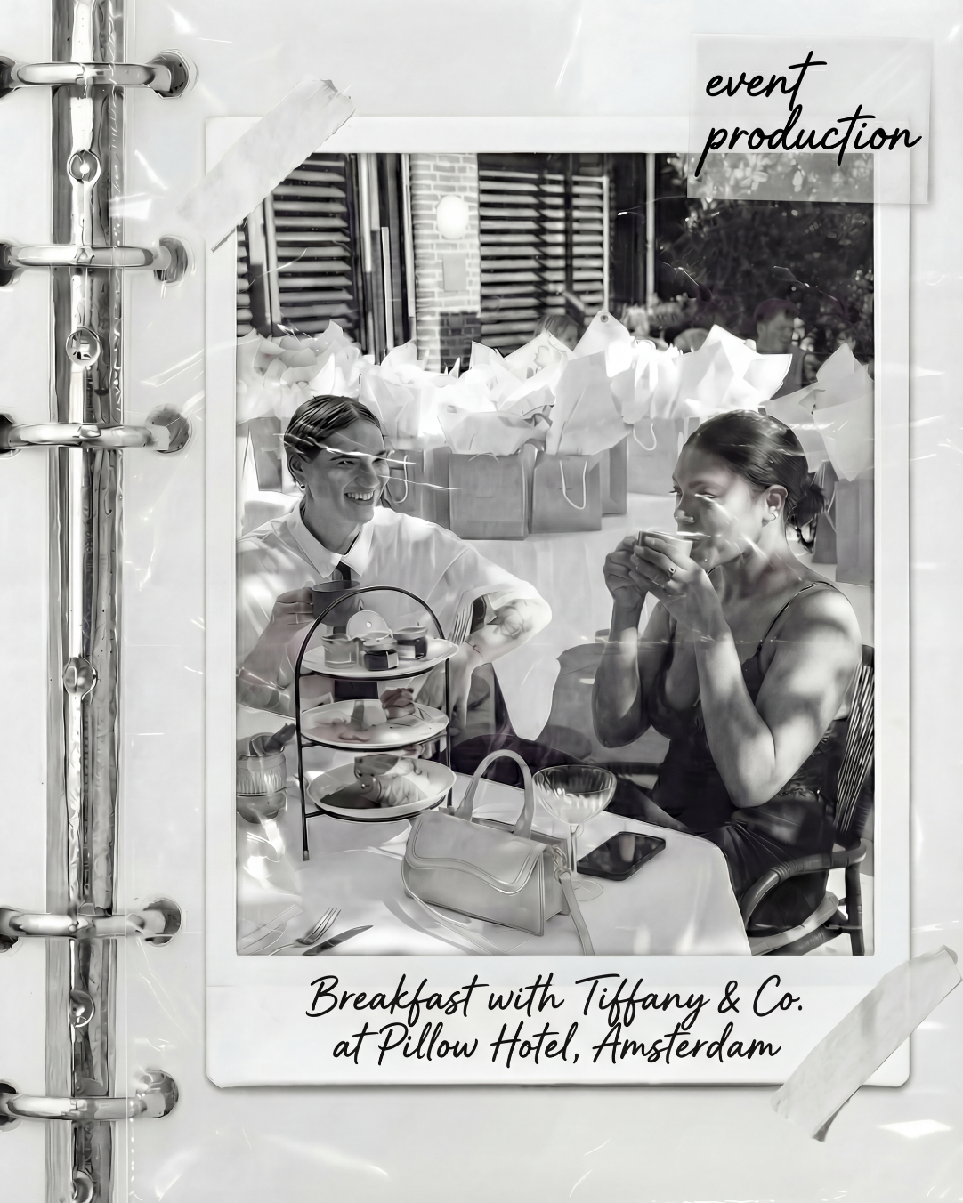 Black and white photo of two women having breakfast at a hotel, one smiling and the other drinking from a cup, with a table set with tea, a handbag, and a three-tier serving tray, taken at Pillow Hotel, Amsterdam.