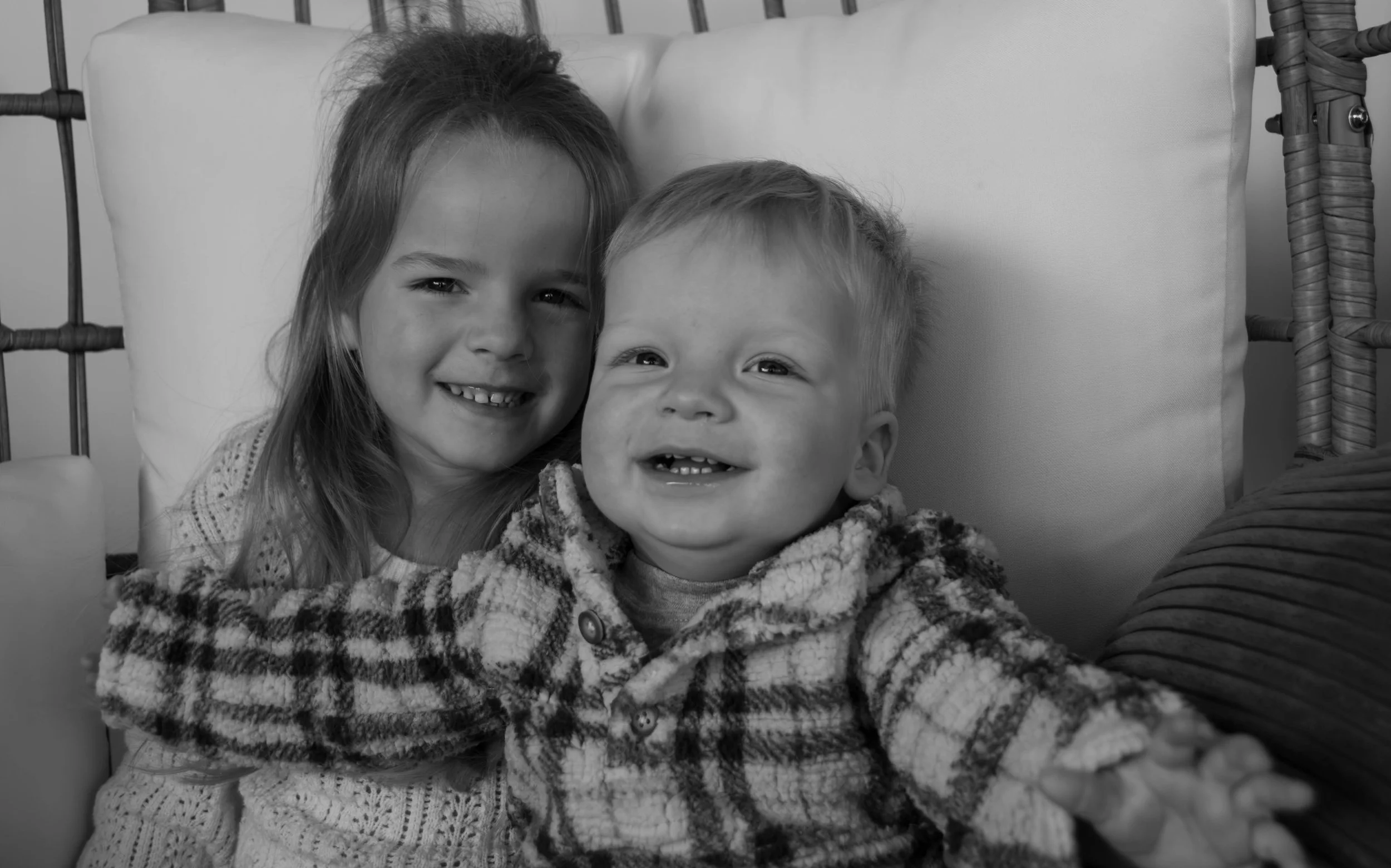 Two young children, a girl and a boy, smiling and hugging each other while sitting on a couch.