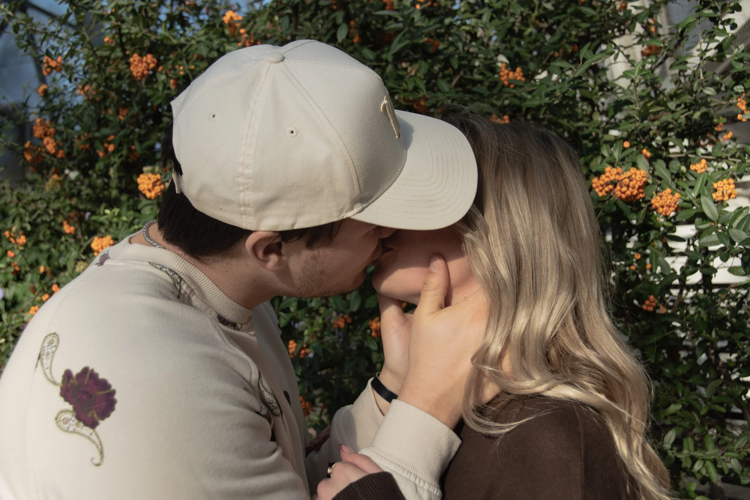 A couple sharing a kiss outdoors surrounded by orange flowers and greenery at the Mitchell Domes in Milwaukee, WI.