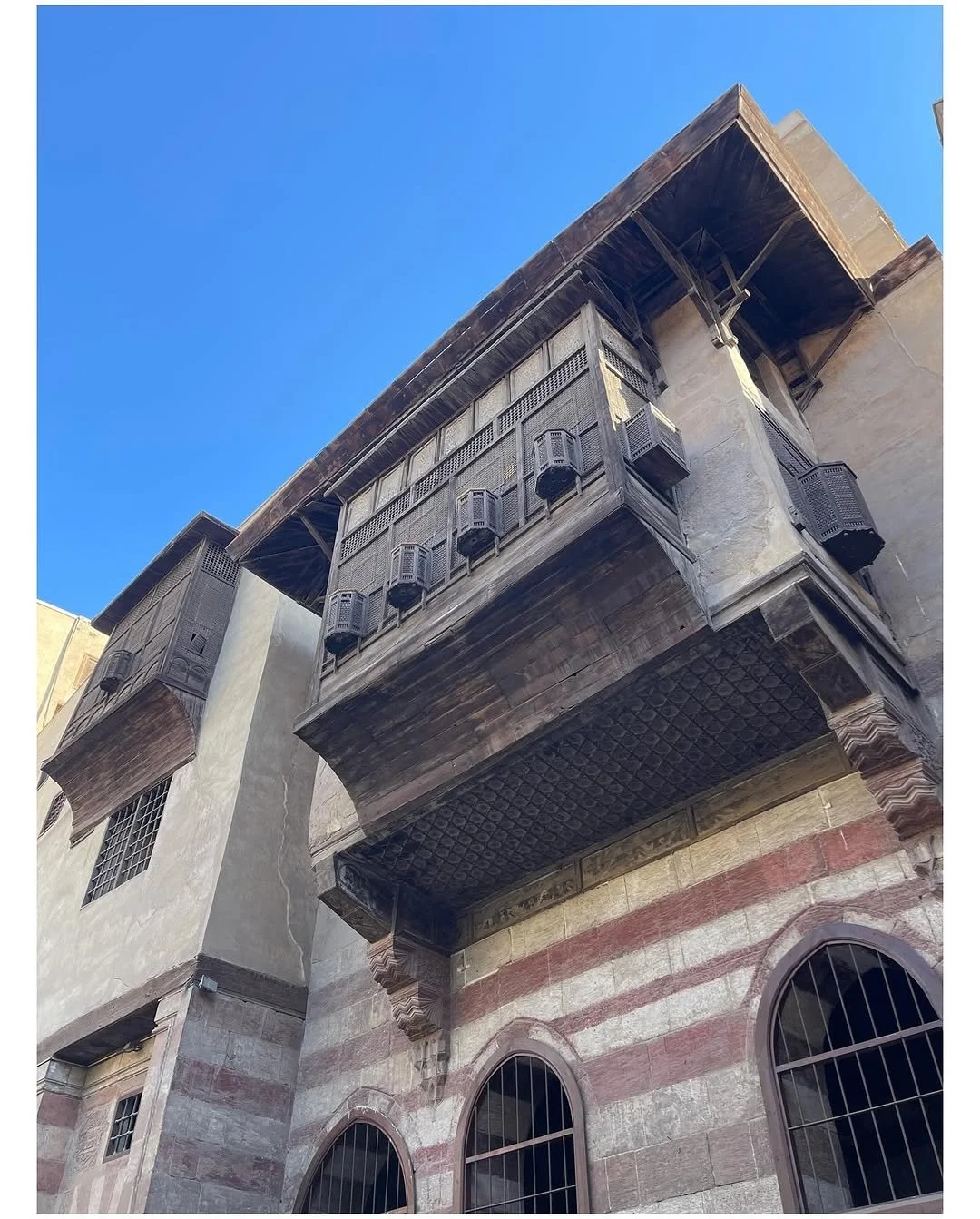 Historic building with a carved stone facade, wooden balconies, and arched windows under a clear blue sky.