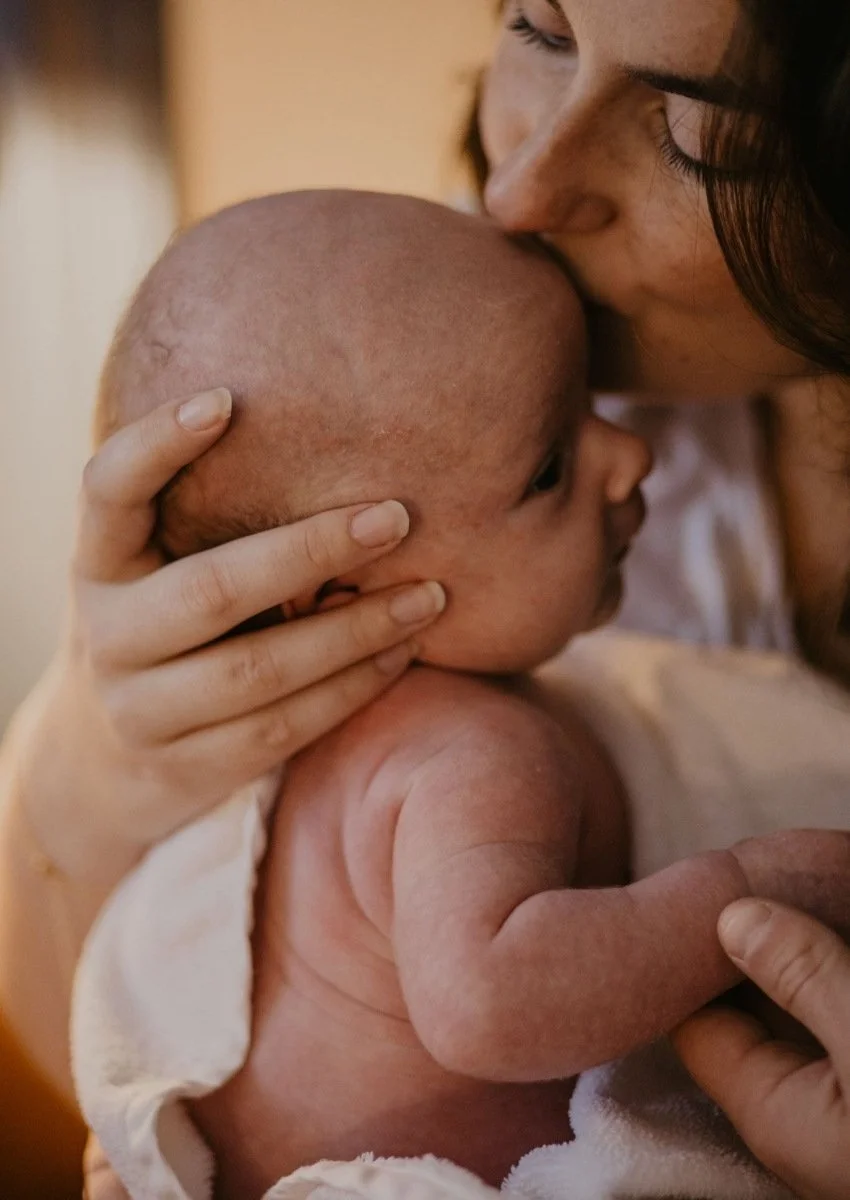 Une femme donne un bisous sur le front à un bébé nue, offrant un moment d'amour et de tendresse.