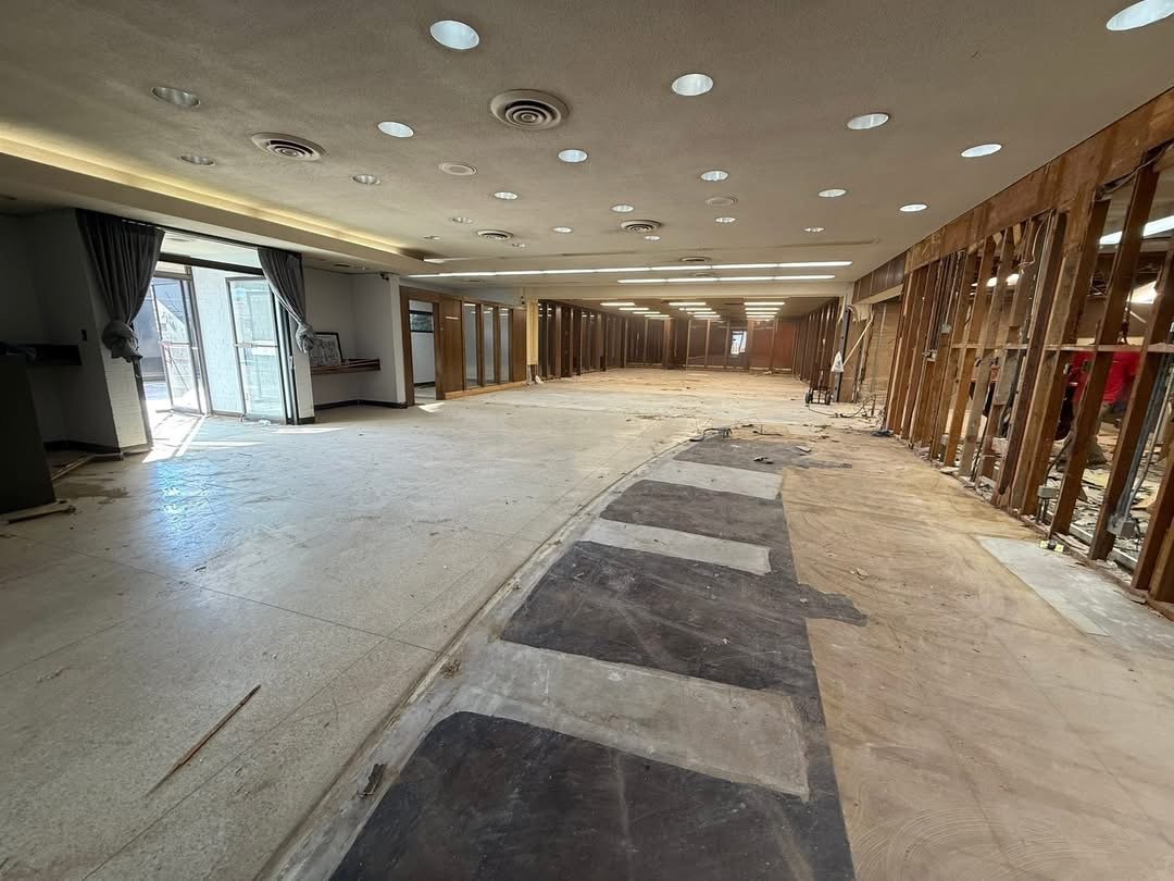 Interior of a room under renovation or construction, with partial flooring removed, construction materials, and exposed wall framing.