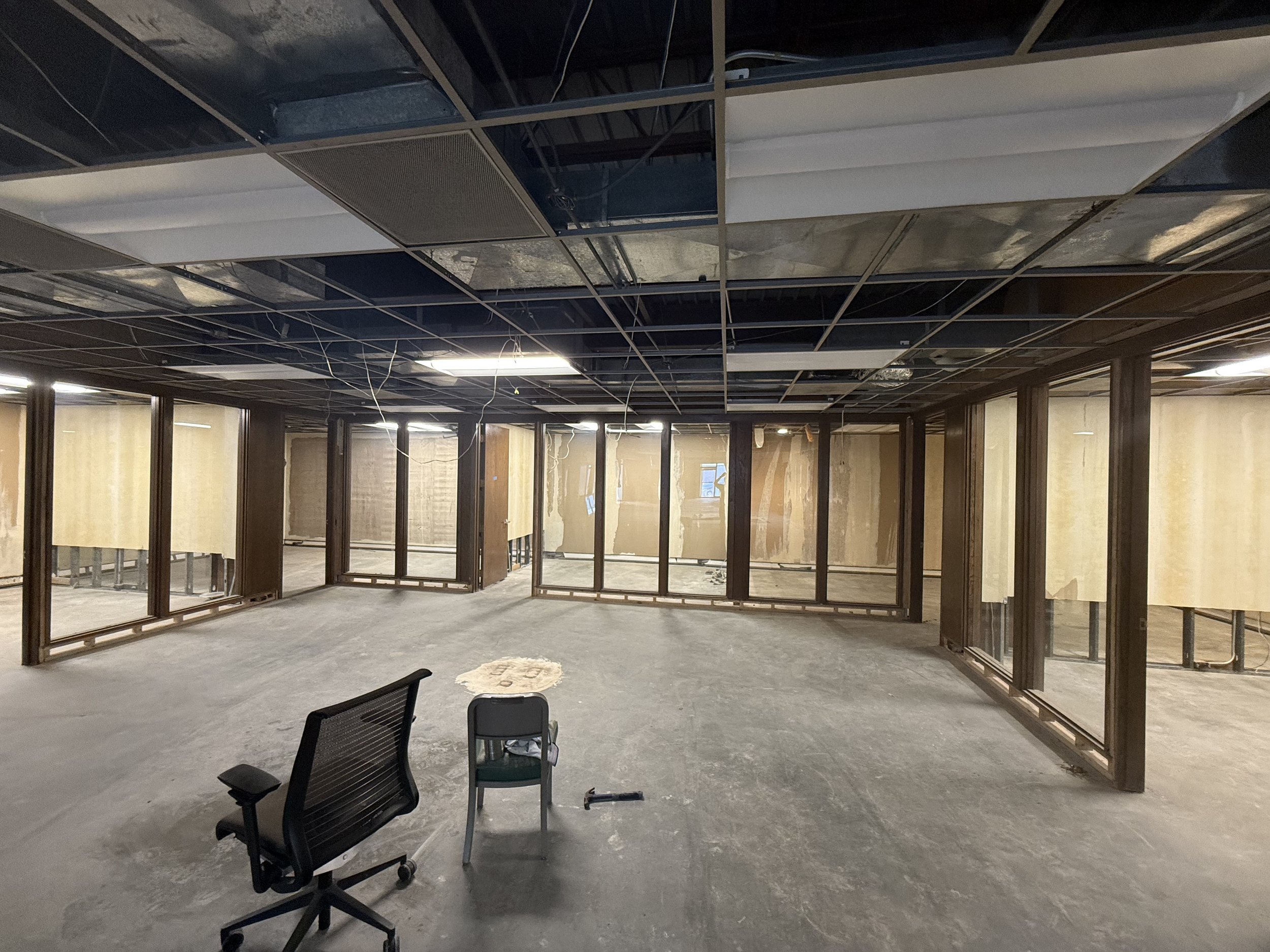 Construction site of an office with unfinished walls, ceiling framework, and construction tools on the floor.