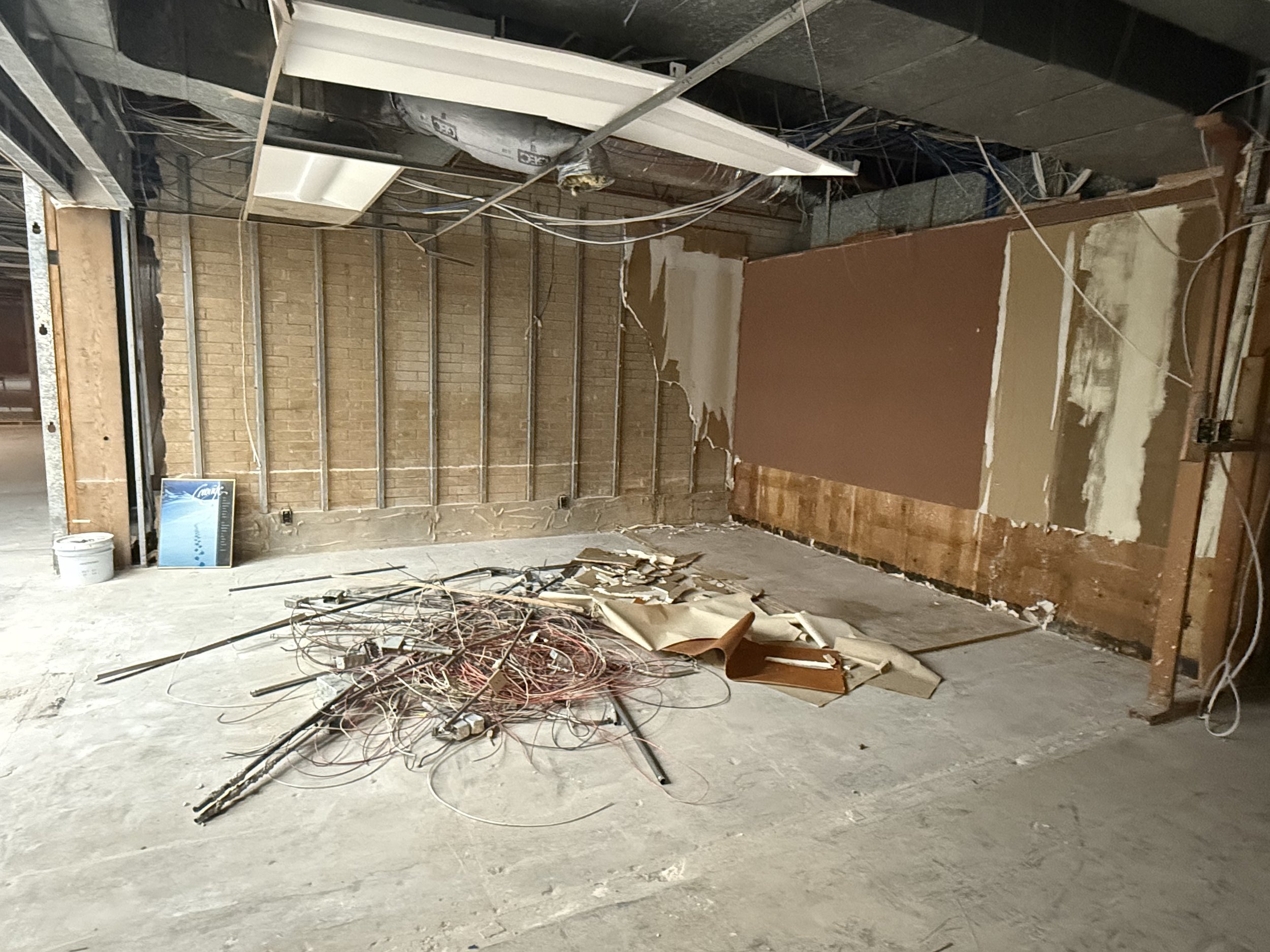 Interior of a room under renovation with exposed brick walls, damaged drywall, scattered wires and construction debris on the floor.