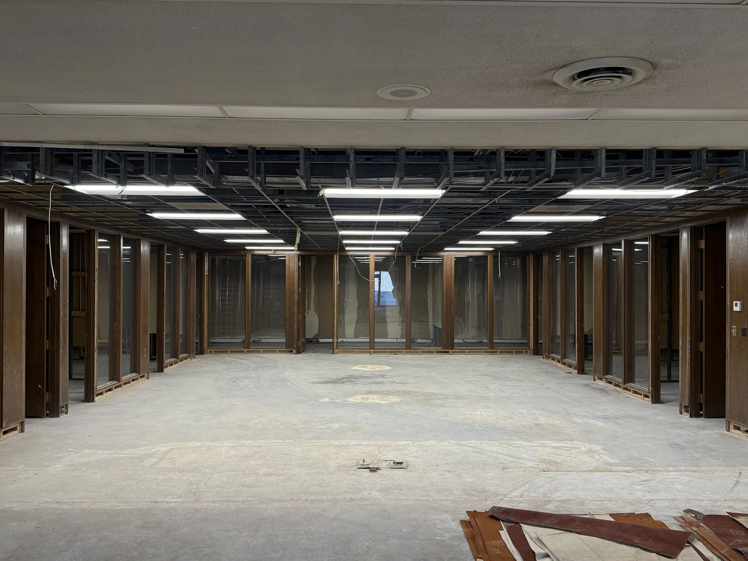 Empty office space under construction with exposed wooden framing and suspended ceiling panels.