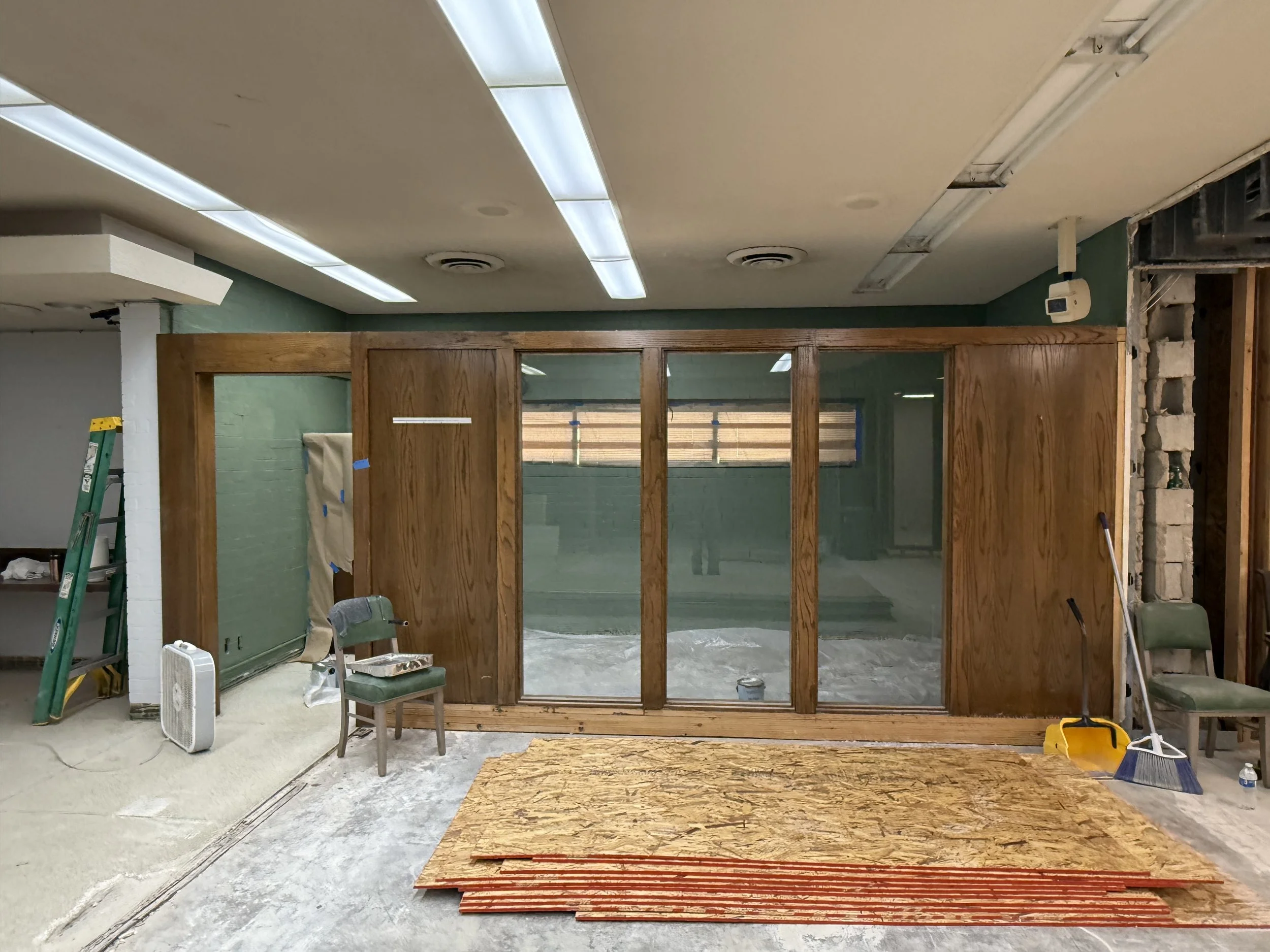 Construction site with wooden framing, glass panels, construction tools, chairs, and supplies in progress.