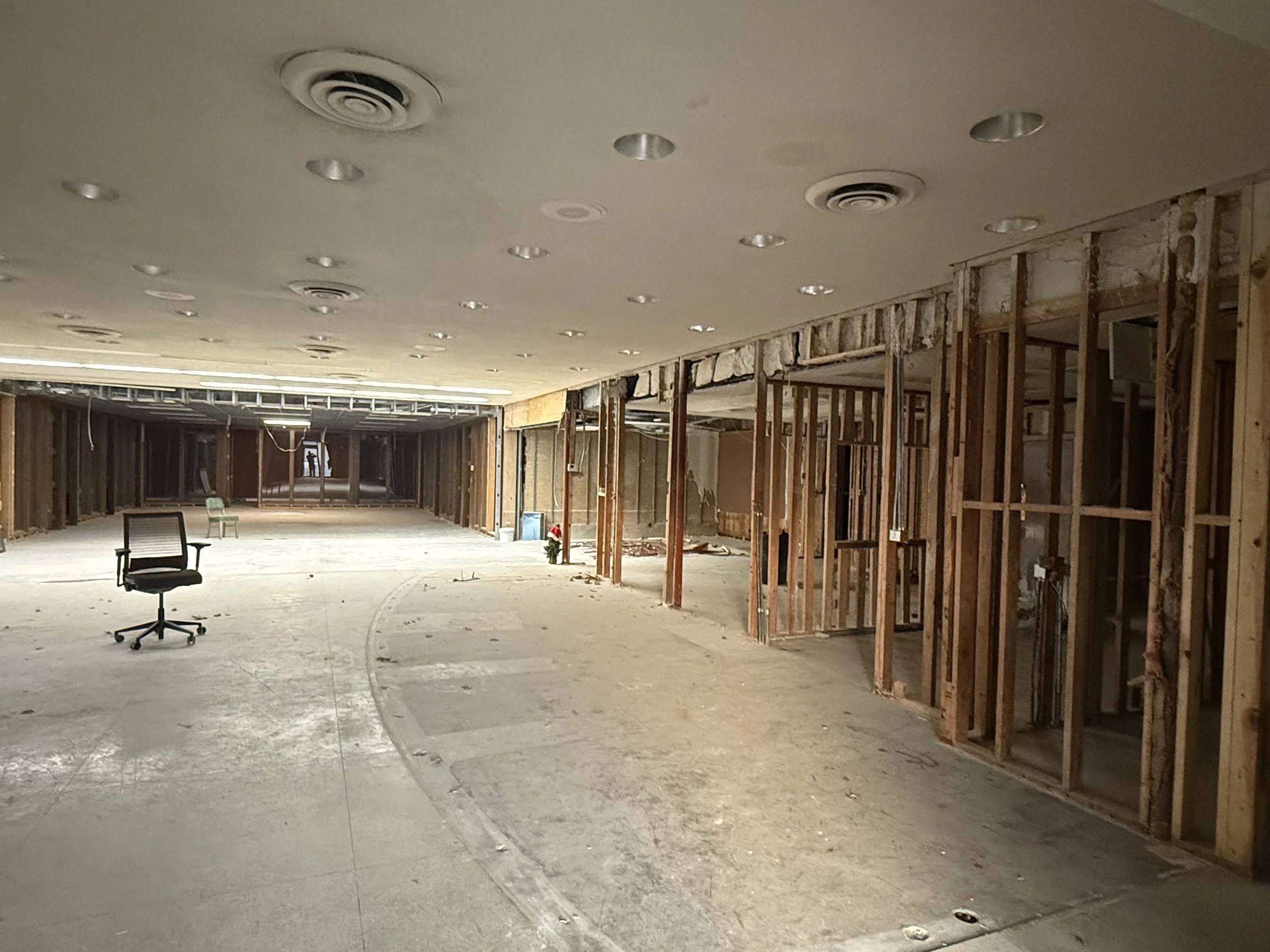 Office space under renovation with exposed wooden framing, an office chair, and construction debris on the floor.