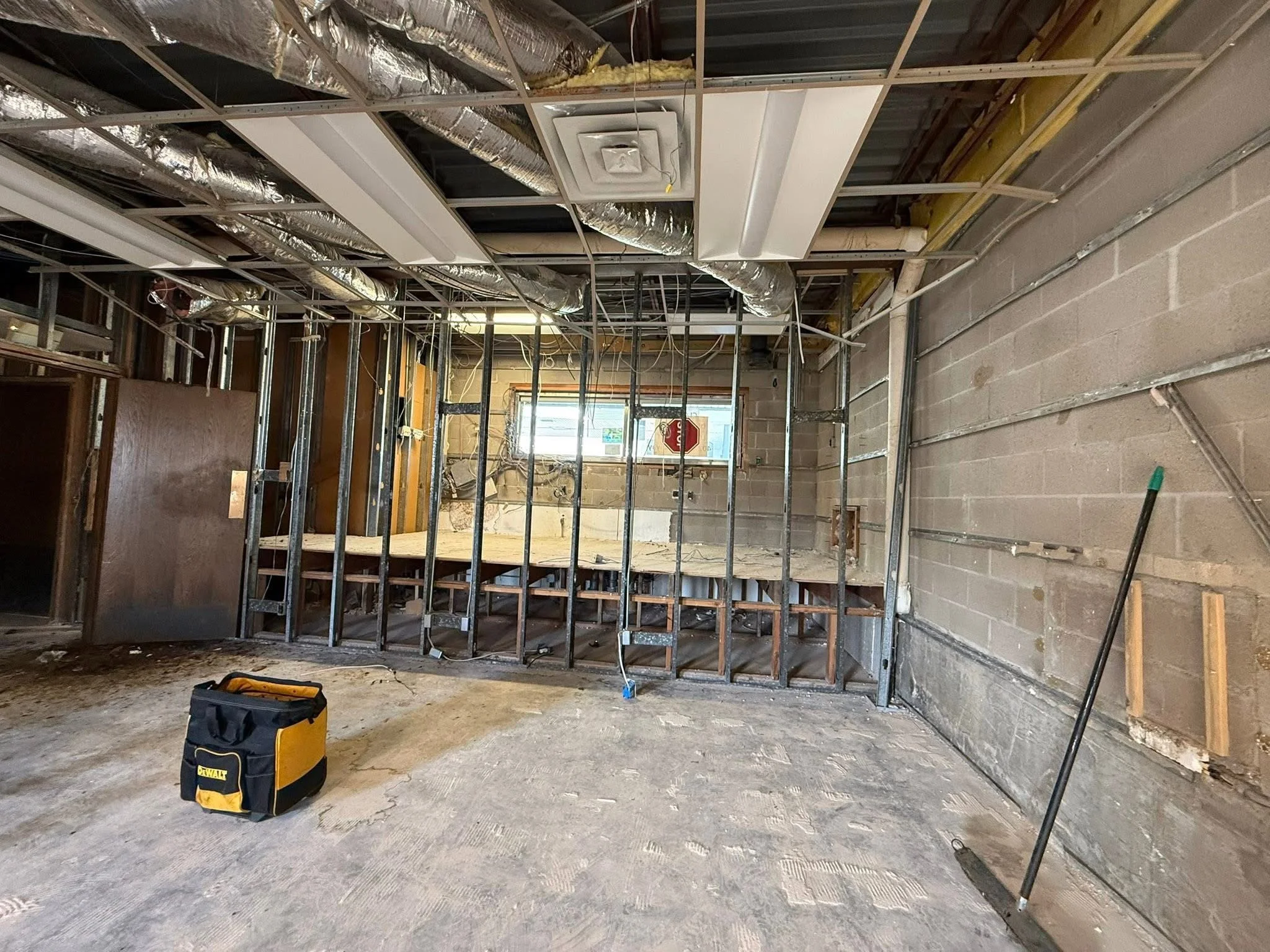 Interior of a building under renovation with exposed framing, ductwork, tools, and a partially framed wall.