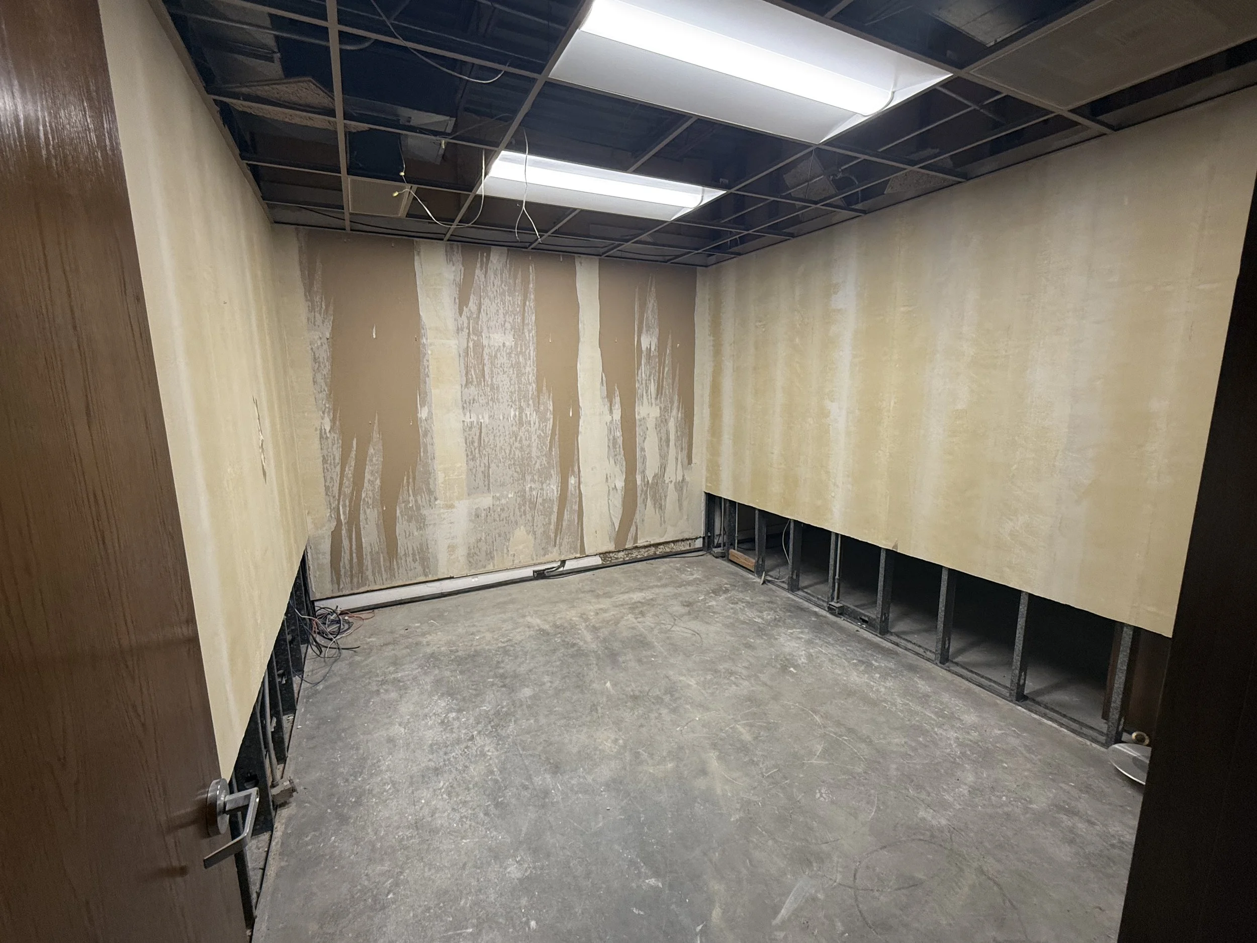 Empty office room under renovation with unfinished drywall and exposed ceiling wiring.