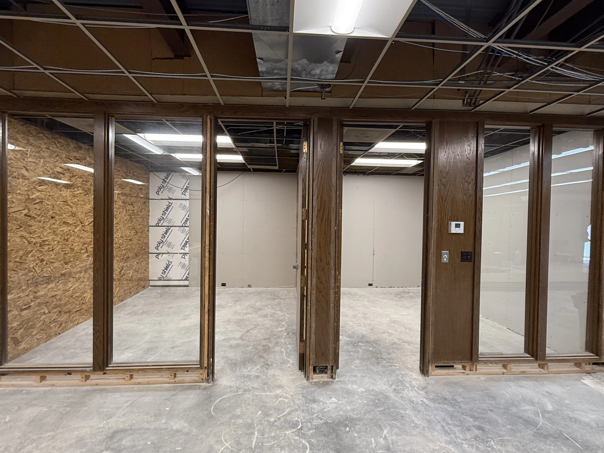 Interior of a room under construction with wood framing, glass walls, and incomplete ceiling with exposed wiring.