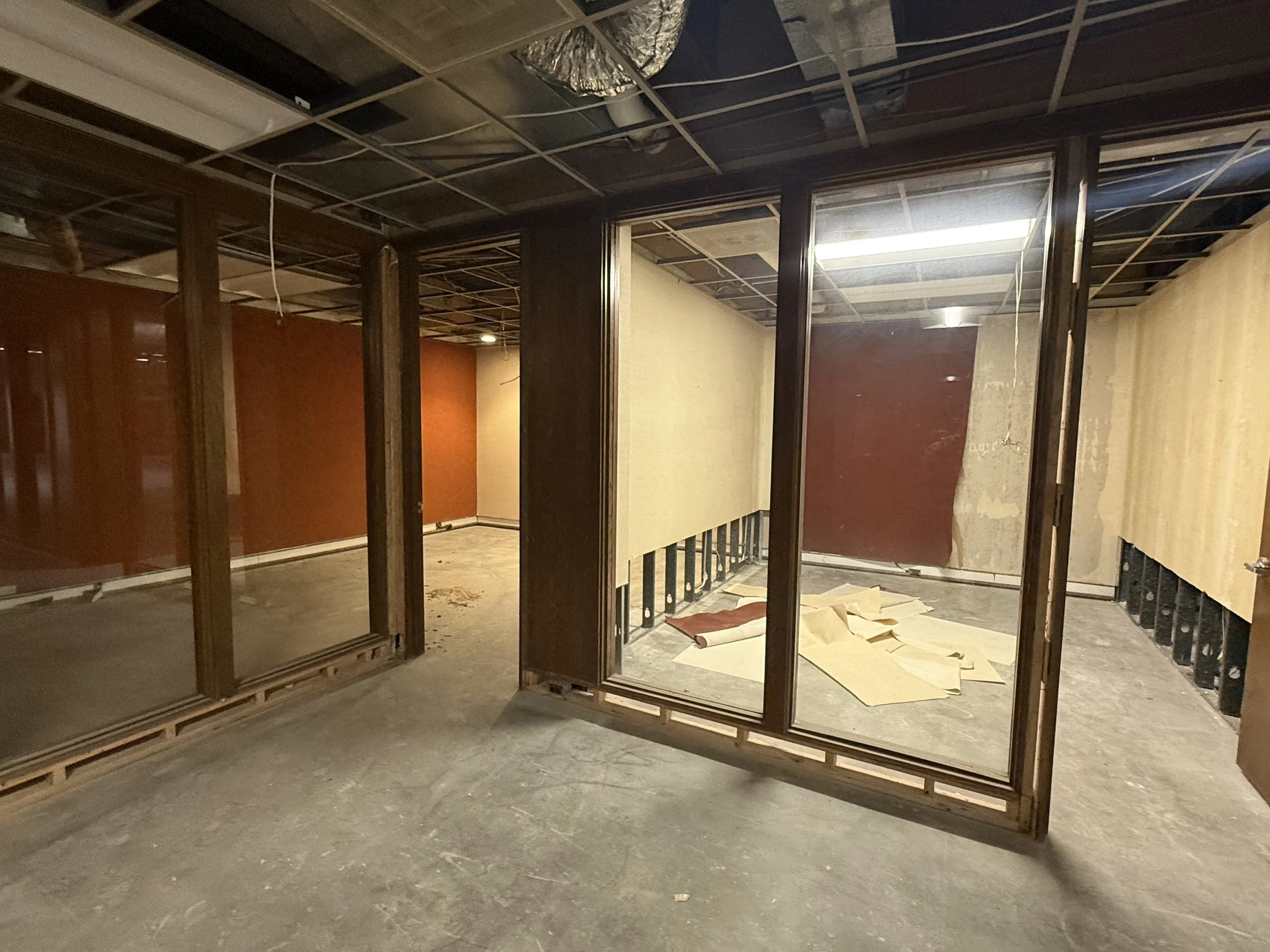 Interior of a building under renovation with exposed walls and ceiling framing, partially finished walls with brown and yellow panels, and construction debris on the floor.