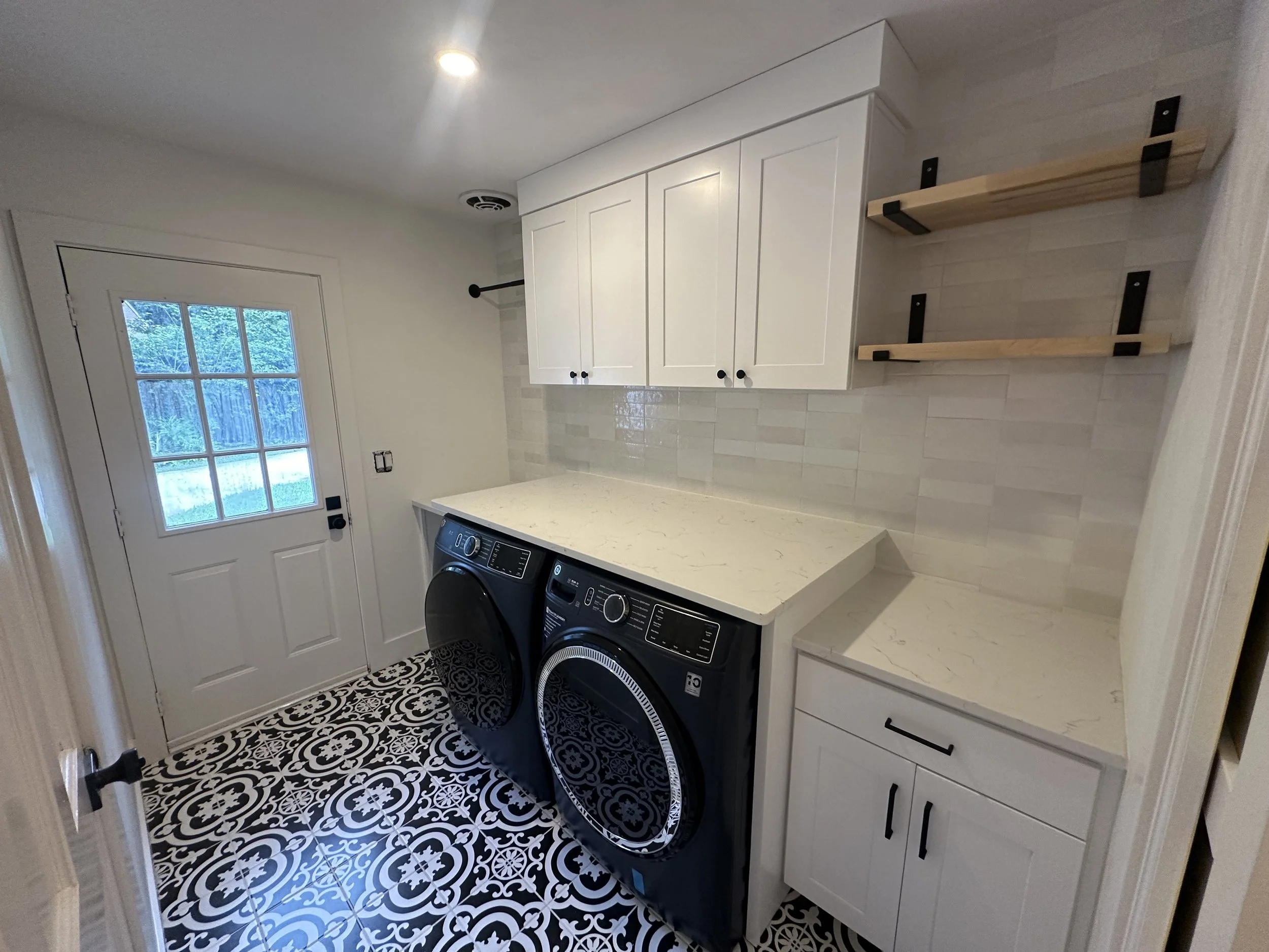 Laundry room Remodel with custom laundry workstation, white cabinets,  new glass pocket door,  floor tiles installed, and two wooden shelves. for a full home remodel that we completed in 2023 in Ormond Beach Florida 