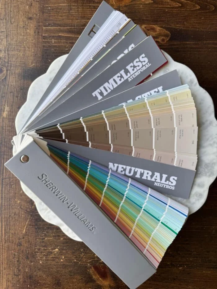 Color palette and paint swatches on a circular fan deck, resting on a white ceramic plate on a wooden surface.