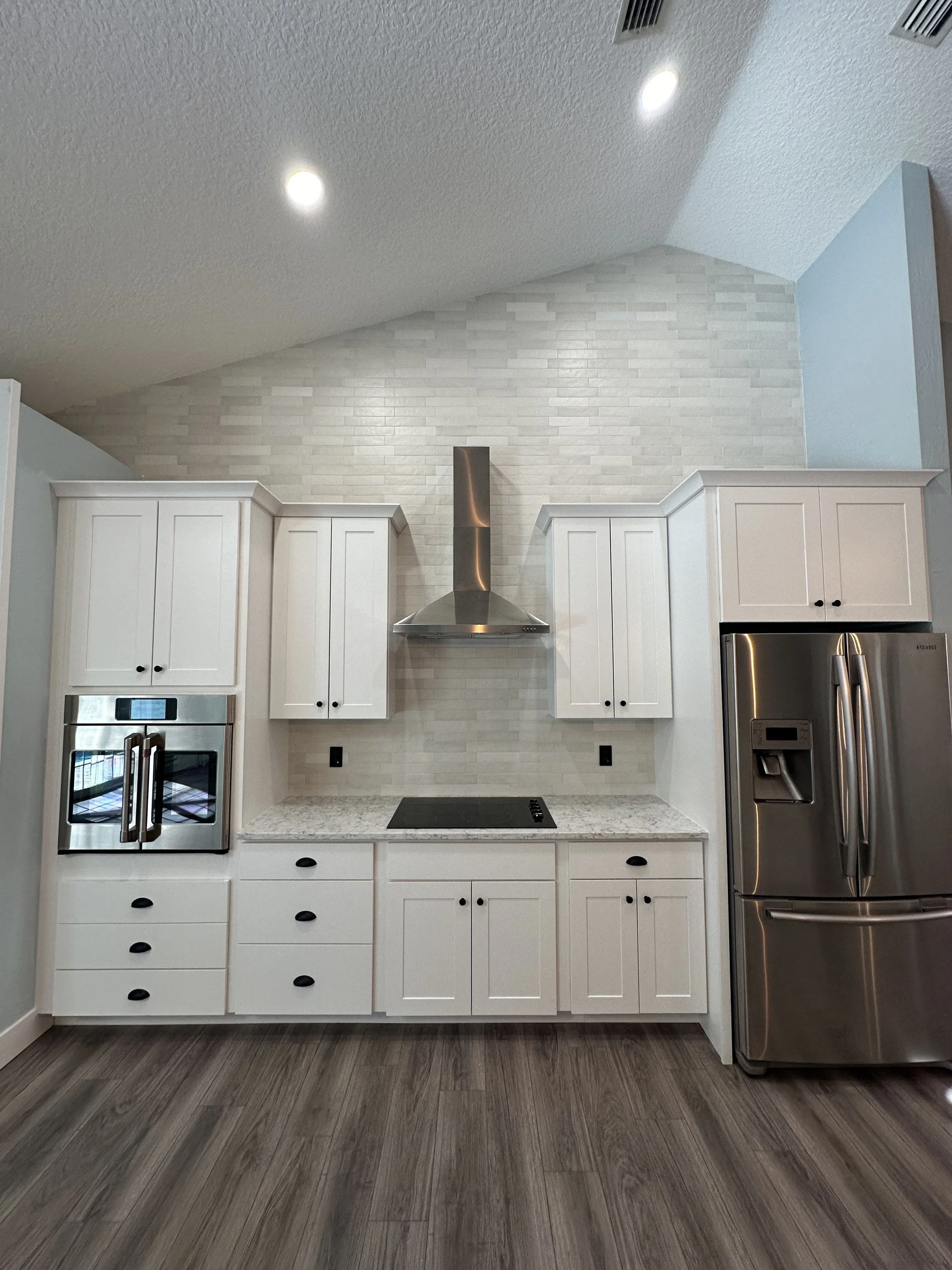 A modern kitchen with white cabinets, stainless steel appliances, a white brick backsplash, and wood laminate flooring.