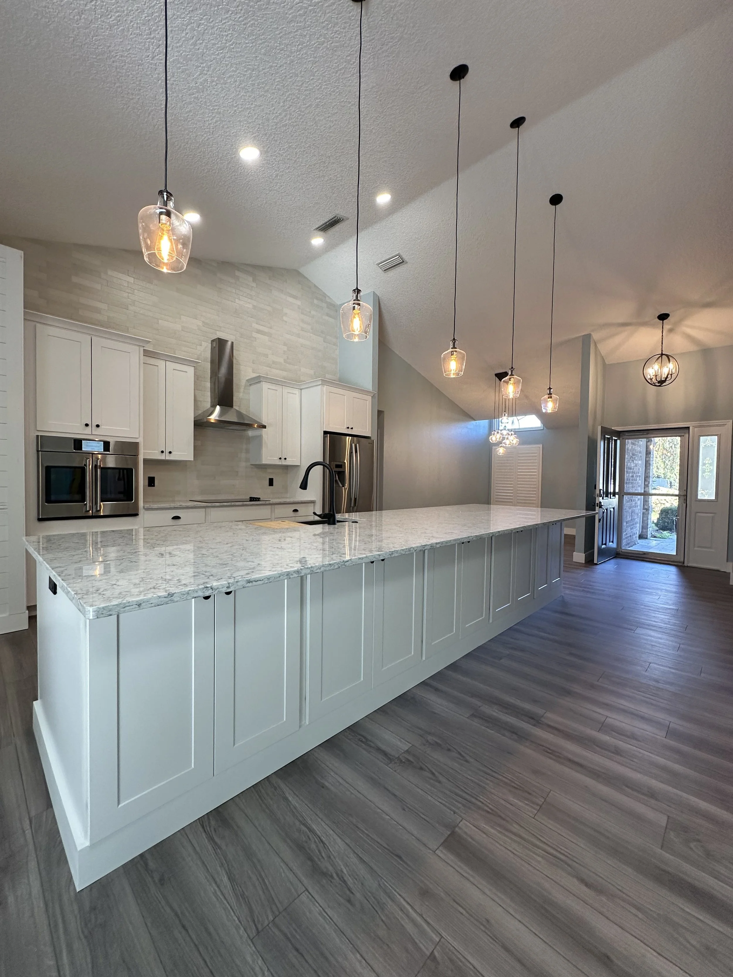 A kitchen Remodel we completed in 2023 in Ormond Beach Florida. With custom white cabinets, Quartz countertops, custom built island, gray LVP flooring, pendant lights, and stainless steel appliances.
