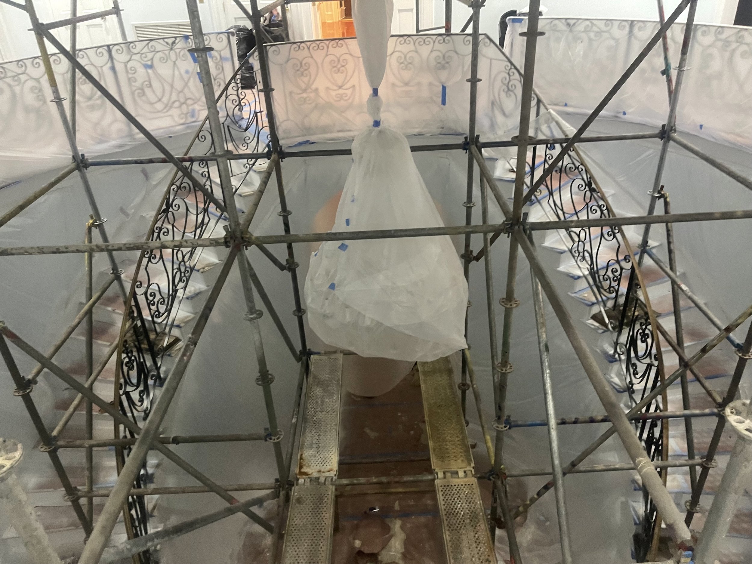 Construction scaffolding surrounding a chandelier covered with plastic in an indoor renovation or decorating project.