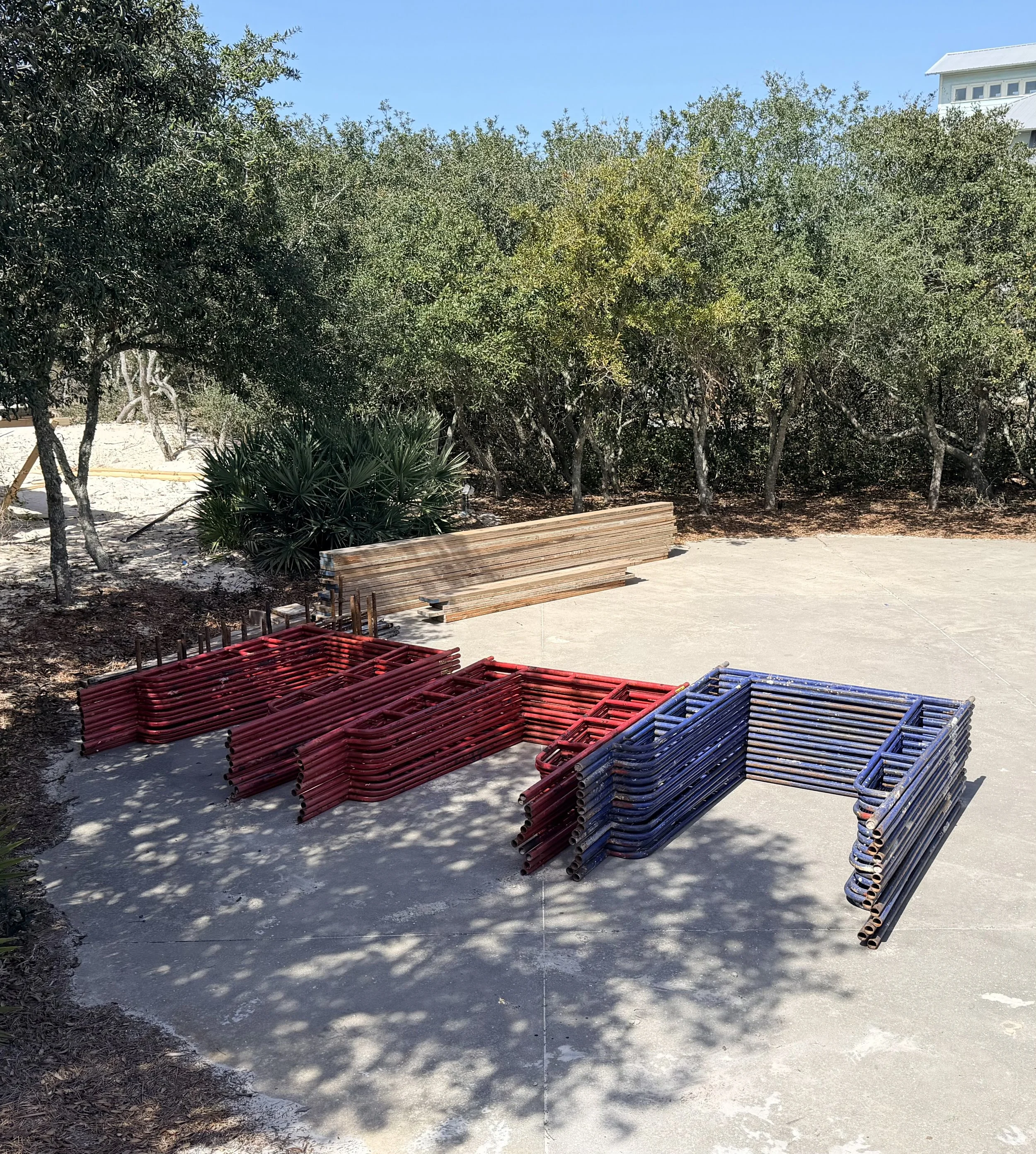 Colorful metal barricades stacked on a concrete sidewalk near some bushes and trees.