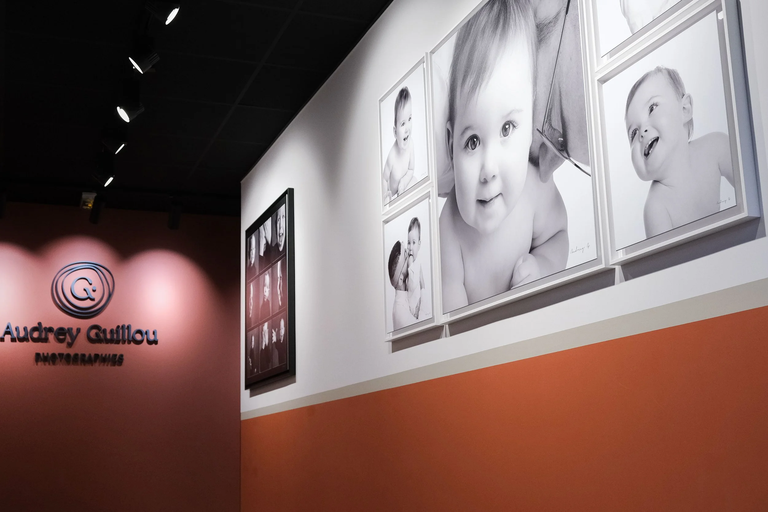 www.studio-photo-vannes.fr Studio audrey Guillou Photographe Vannes morbihan Exposition de portraits en noir et blanc d'enfants dans une galerie avec un mur rose avec le nom 'Audrey Guillou PHOTOGRAPHIES'
