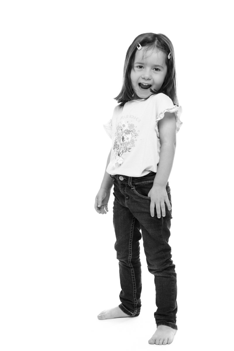 Une jeune fille souriante posant pieds nus sur un fond blanc.