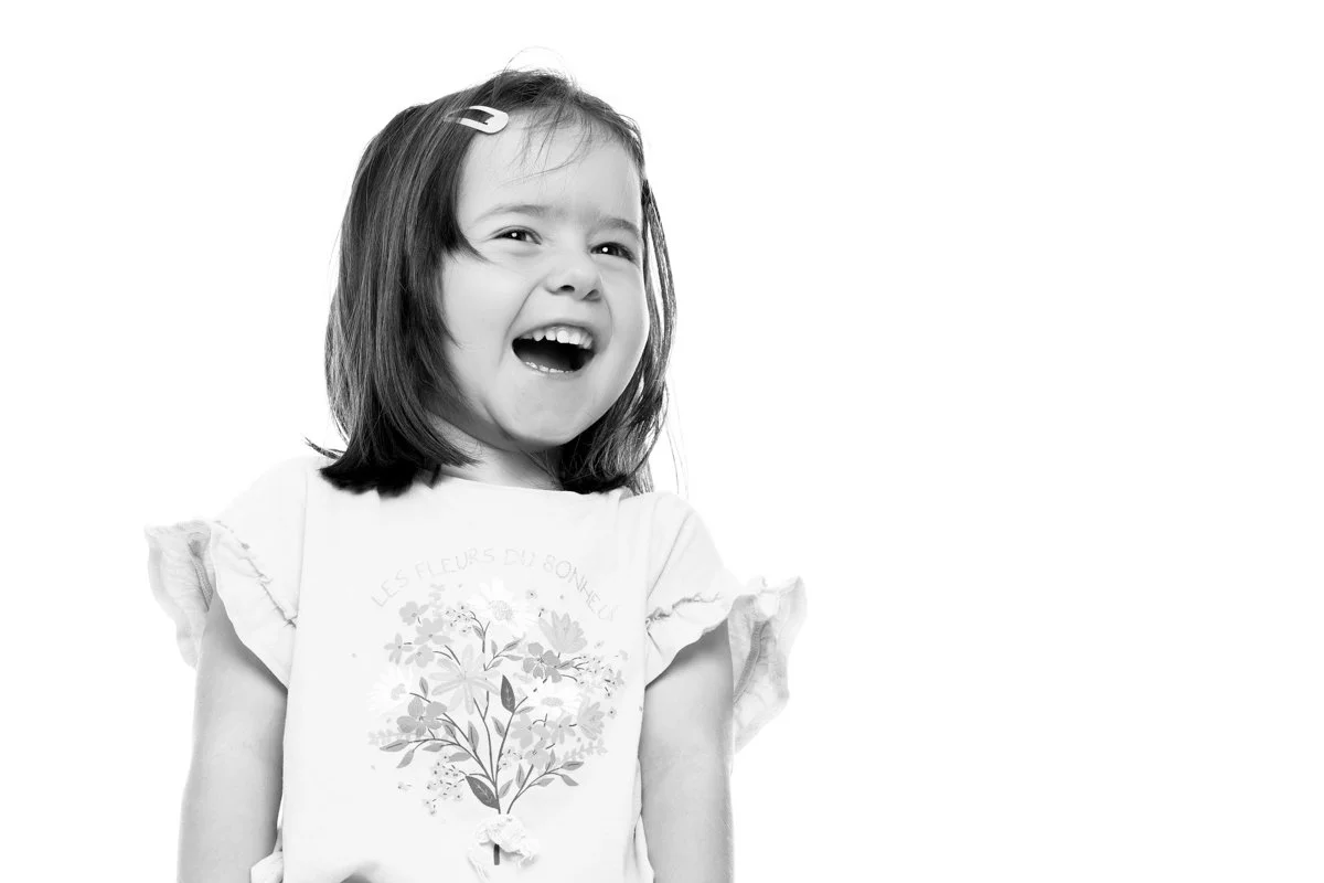 Une jeune fille souriante avec des cheveux bruns, portant une t-shirt avec un dessin de fleurs et un texte en français, dans un fond blanc.