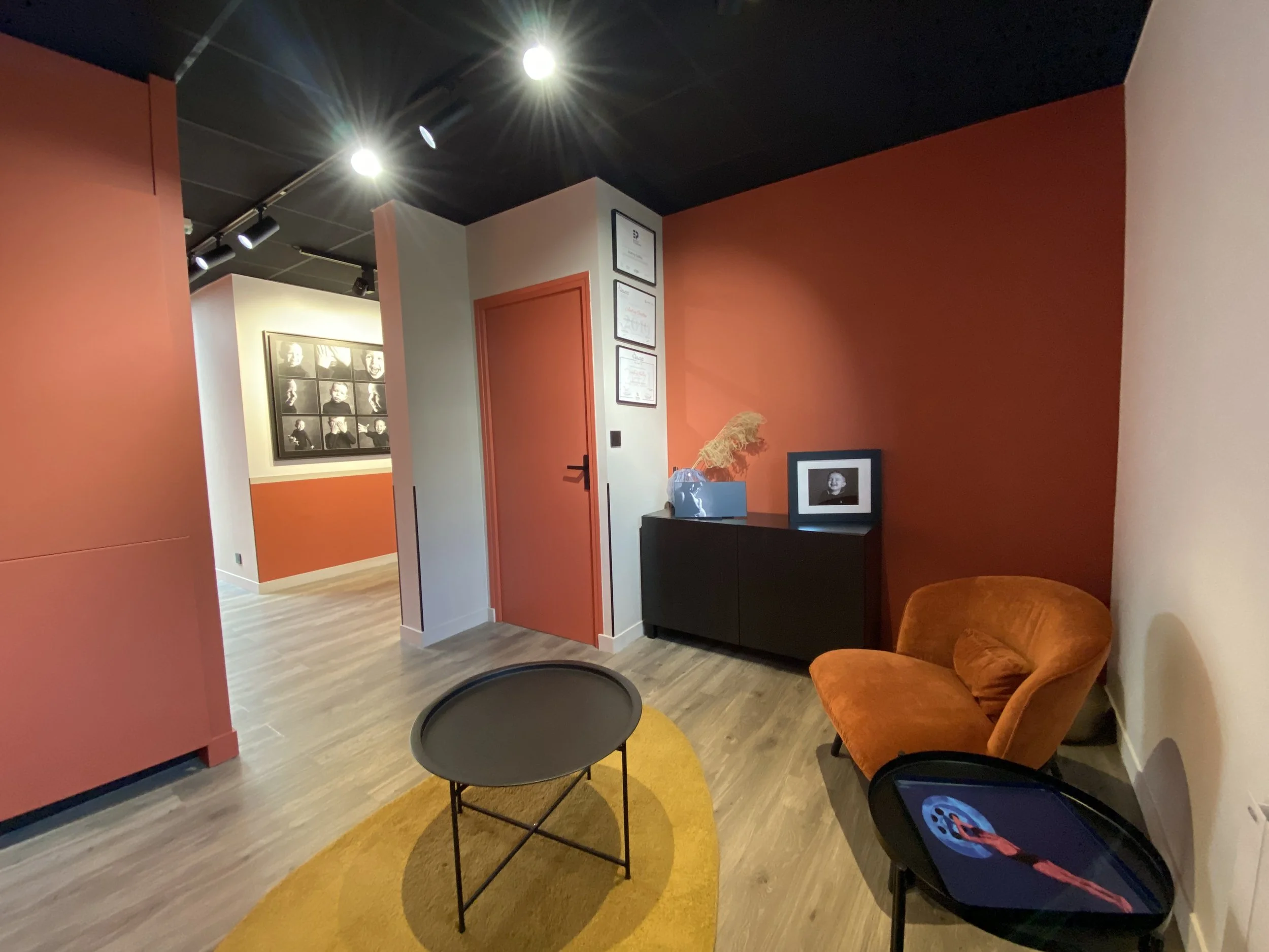 www.studio-photo-vannes.fr Studio audrey Guillou Photographe Vannes morbihan Salle d'attente moderne avec fauteuil orange, table noire, décor neutre, peintures encadrées, et luminaires encastrés au plafond.