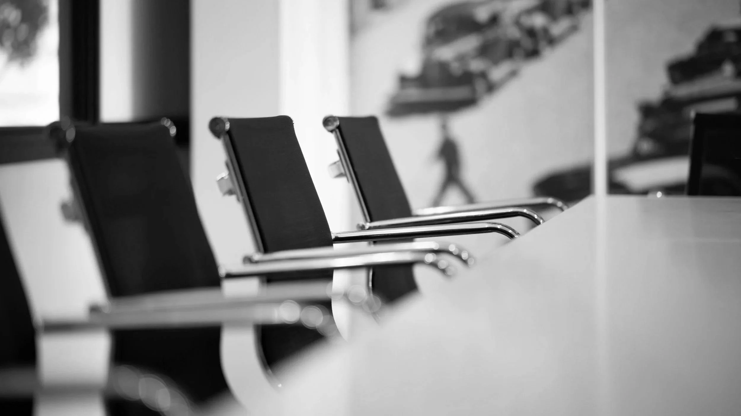 Black and white photo of multiple office chairs arranged along a conference table in a meeting room.
