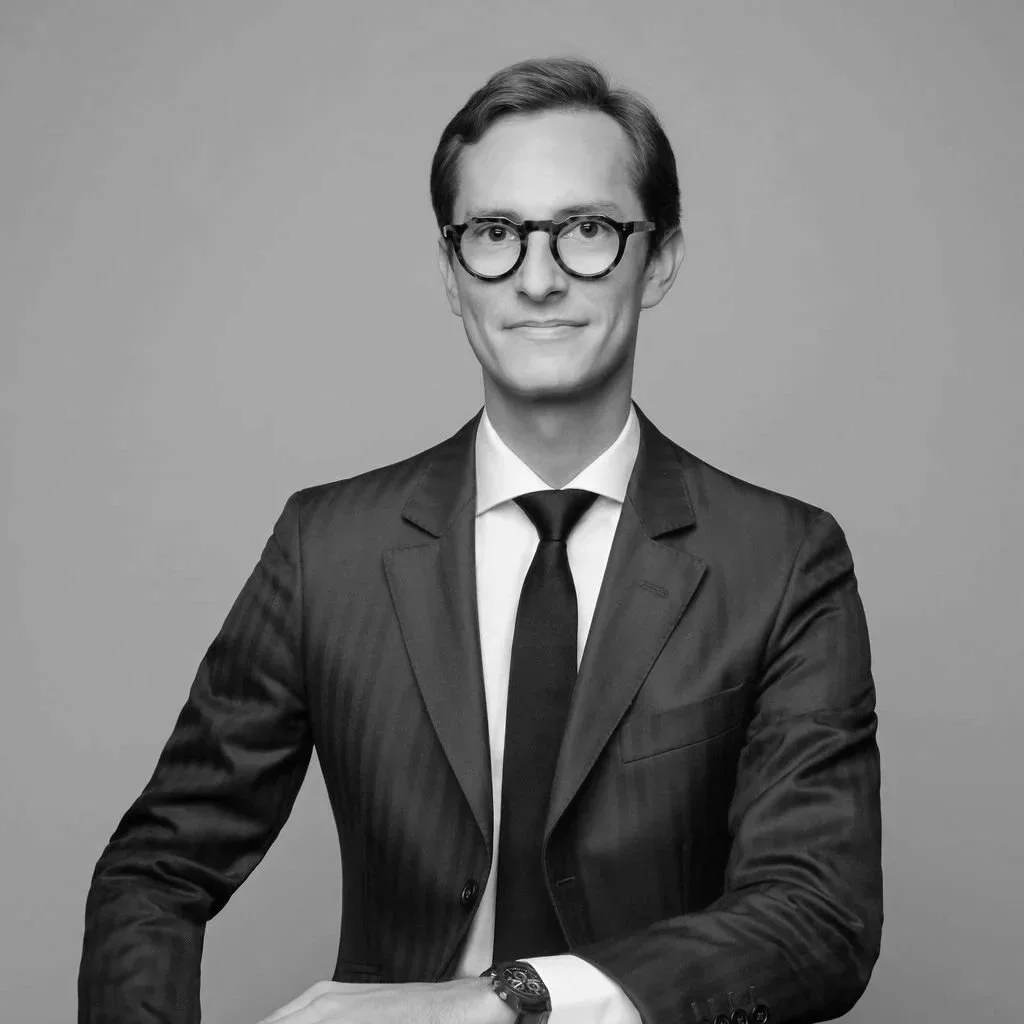 A black and white portrait of a man in a suit and glasses, posing against a plain background.