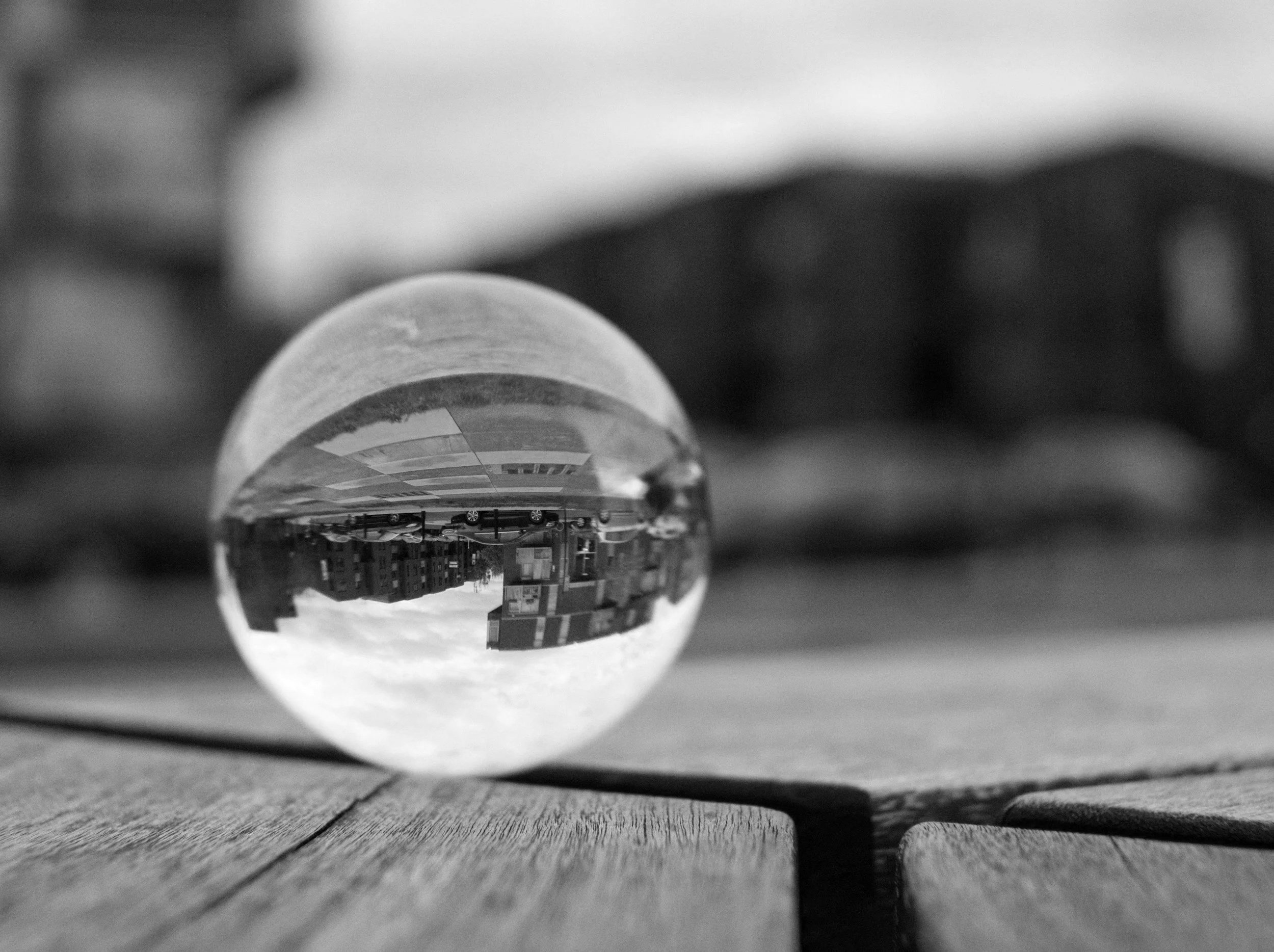 Close-up of the bottom of a glass bottle lying on a wooden surface, with buildings and cars reflected upside down in the glass.