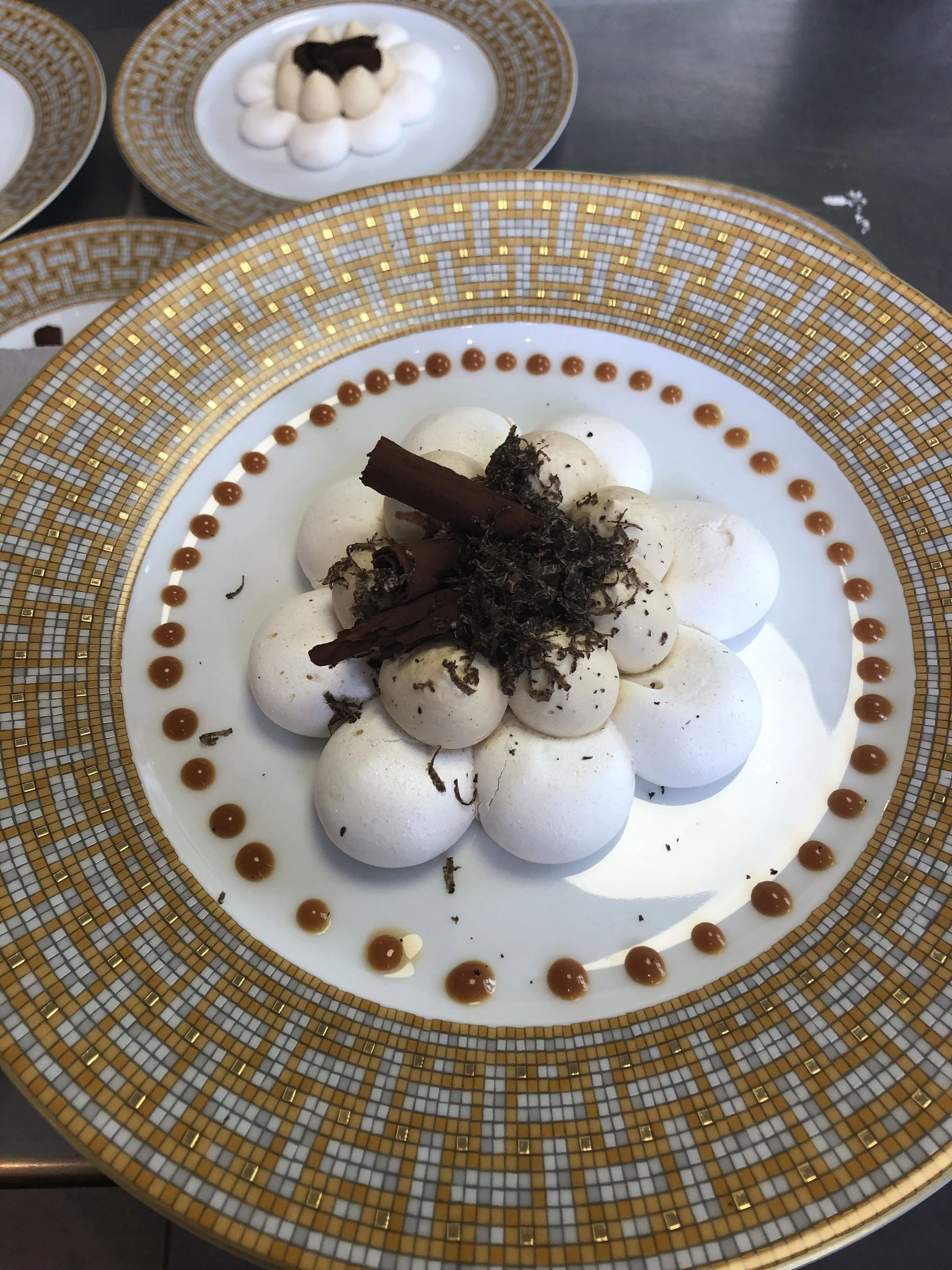 Dessert à base de petites meringues blanches garnies de morceaux de chocolat noir et décoré de points de caramel autour de l'assiette.