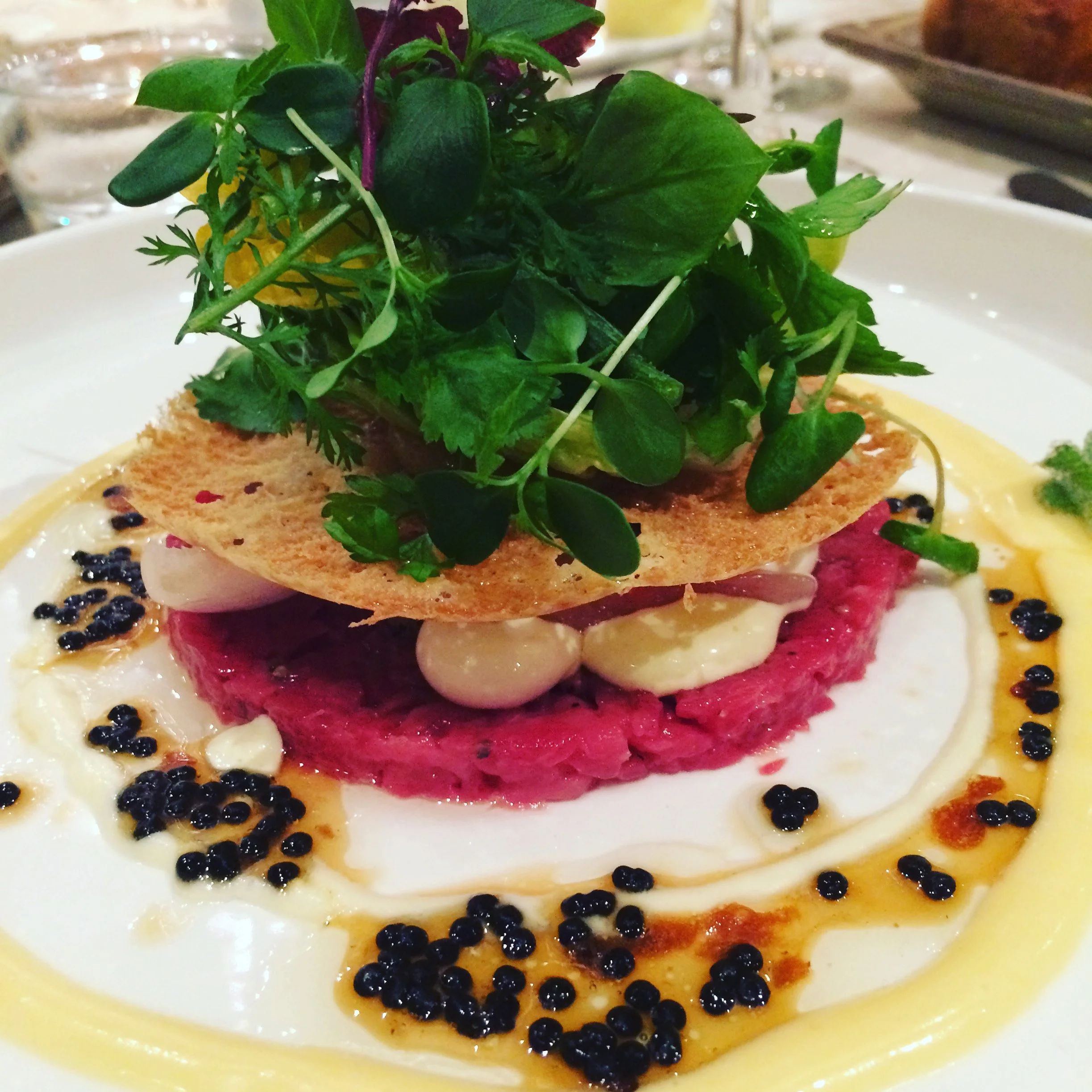 Assiette de tartare de viande avec guacamole, crème, graines de câpres, garnie de salade verte et d'une chips croquante sur le dessus.