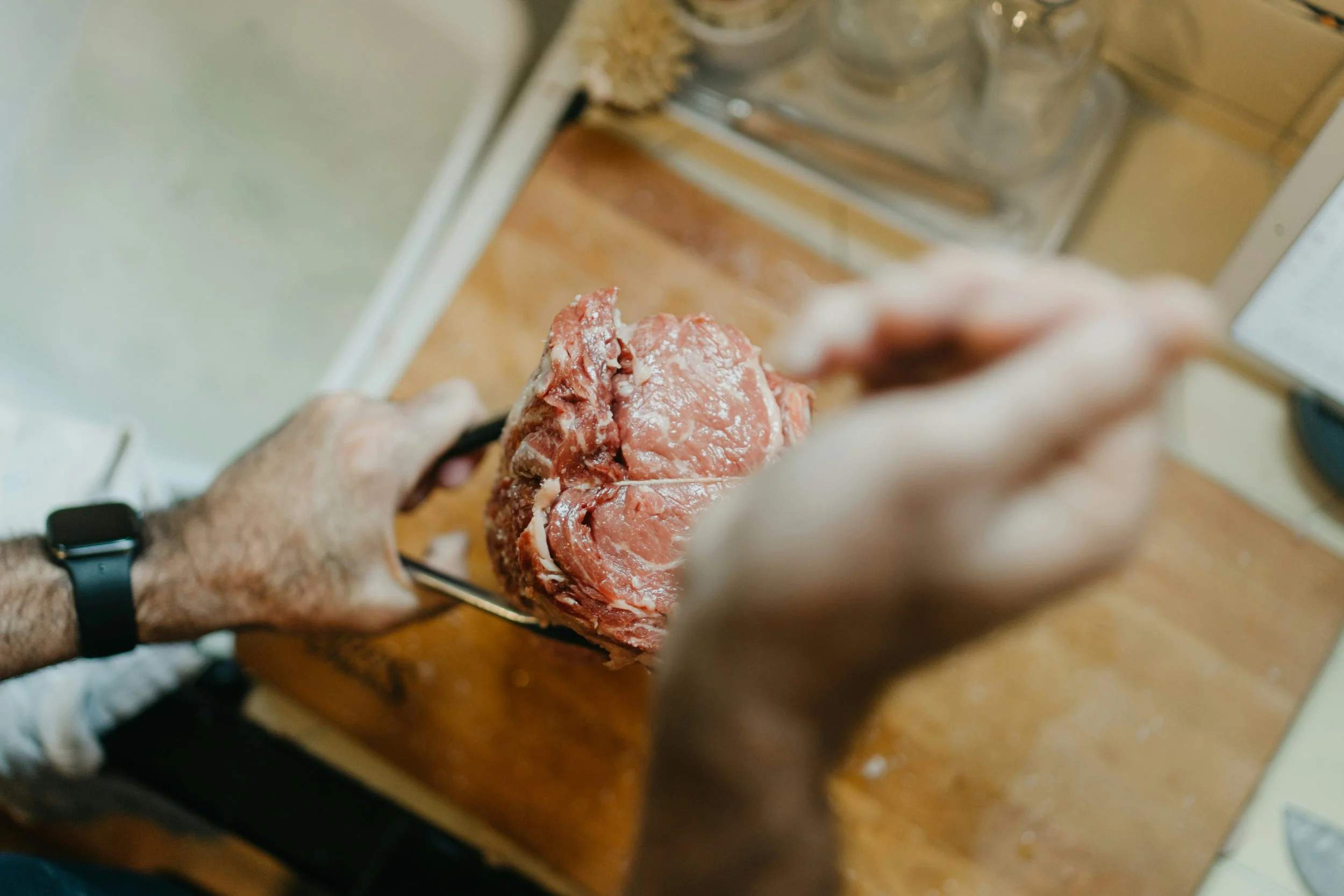 Une personne tenant une pièce de viande crue avec une fourchette sur un plan de travail en bois.