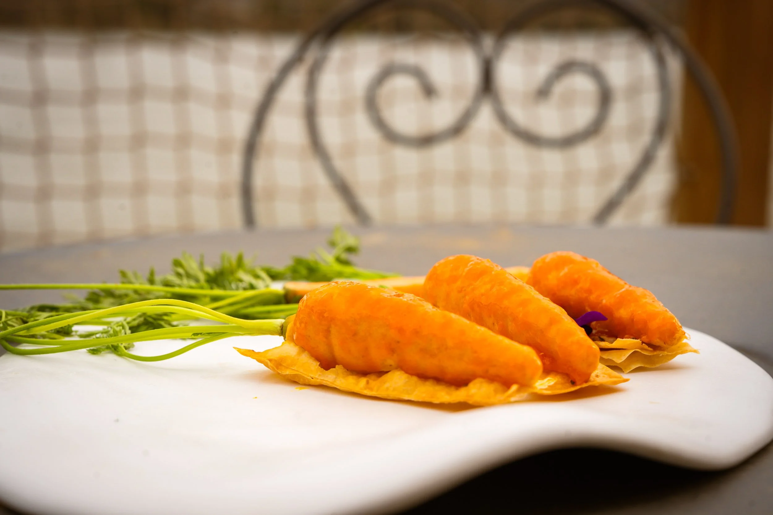 Trois pâtés en croûte orange sur une lamelle, accompagnés de feuilles vertes, sur une assiette blanche dans un décor intérieur.