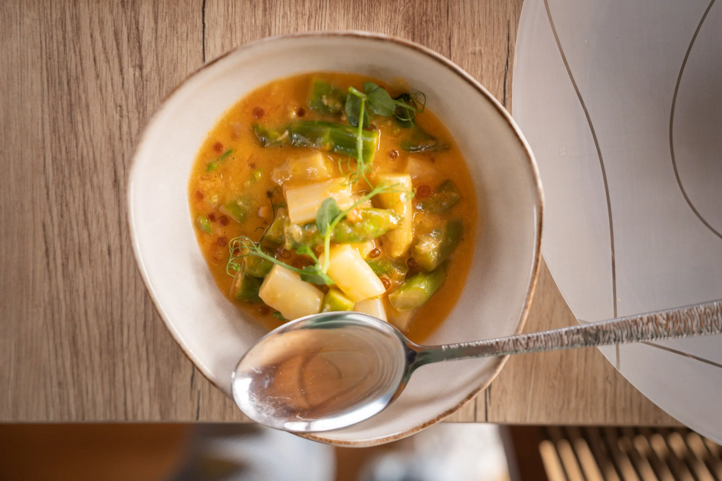 Soupe de légumes avec garniture de légumes verts et herbes, dans un bol blanc sur un plateau en bois.