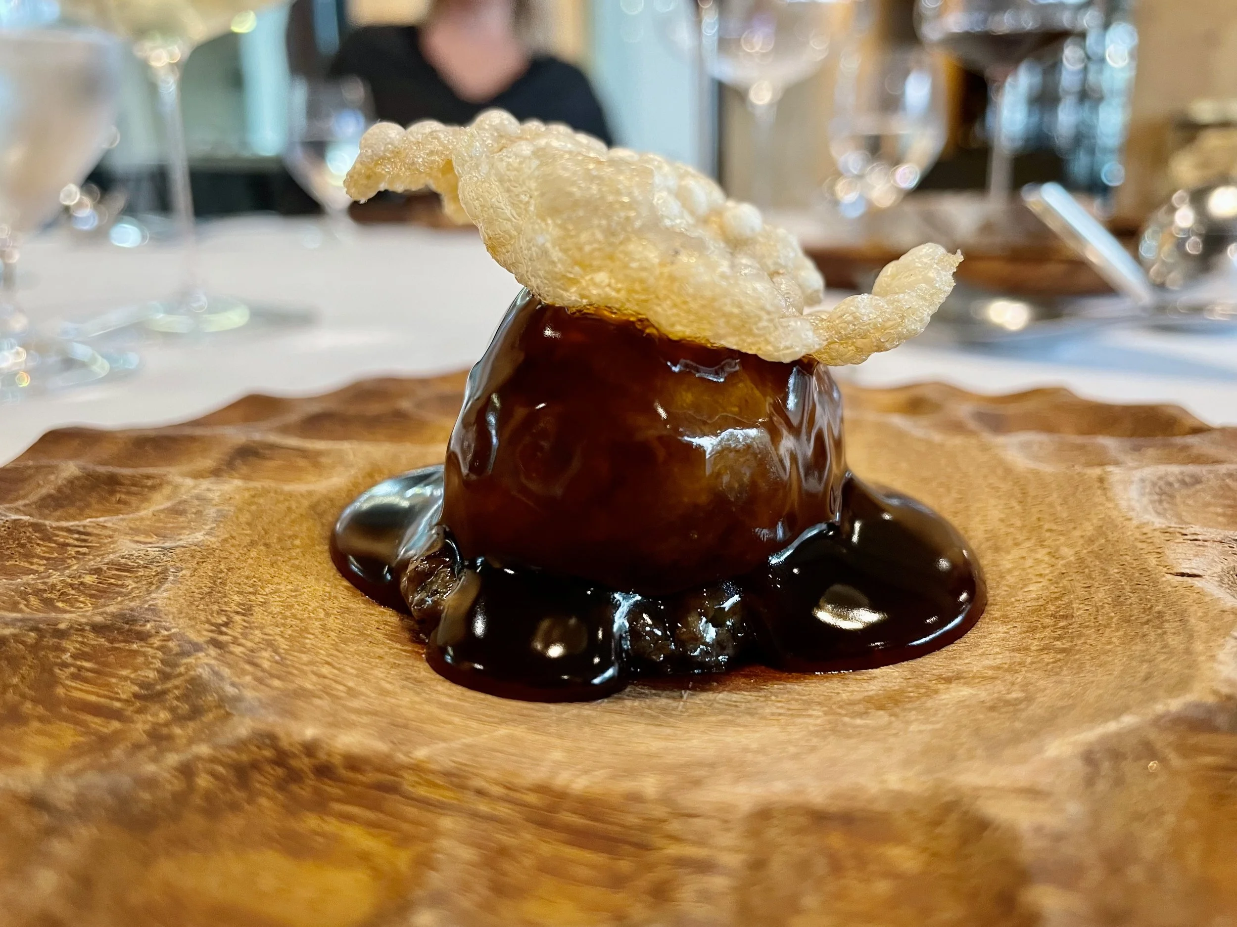 Un dessert gourmand avec une boule de glace recouverte de sauce chocolat fondu, décorée d'une croustade croustillante, présenté sur une assiette en bois.