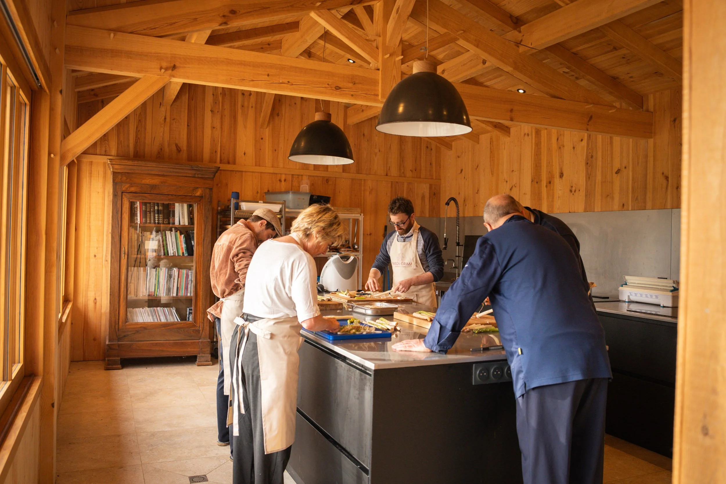 Groupe de personnes en train de cuisiner dans une cuisine en bois avec des lampes noires suspendues au plafond.