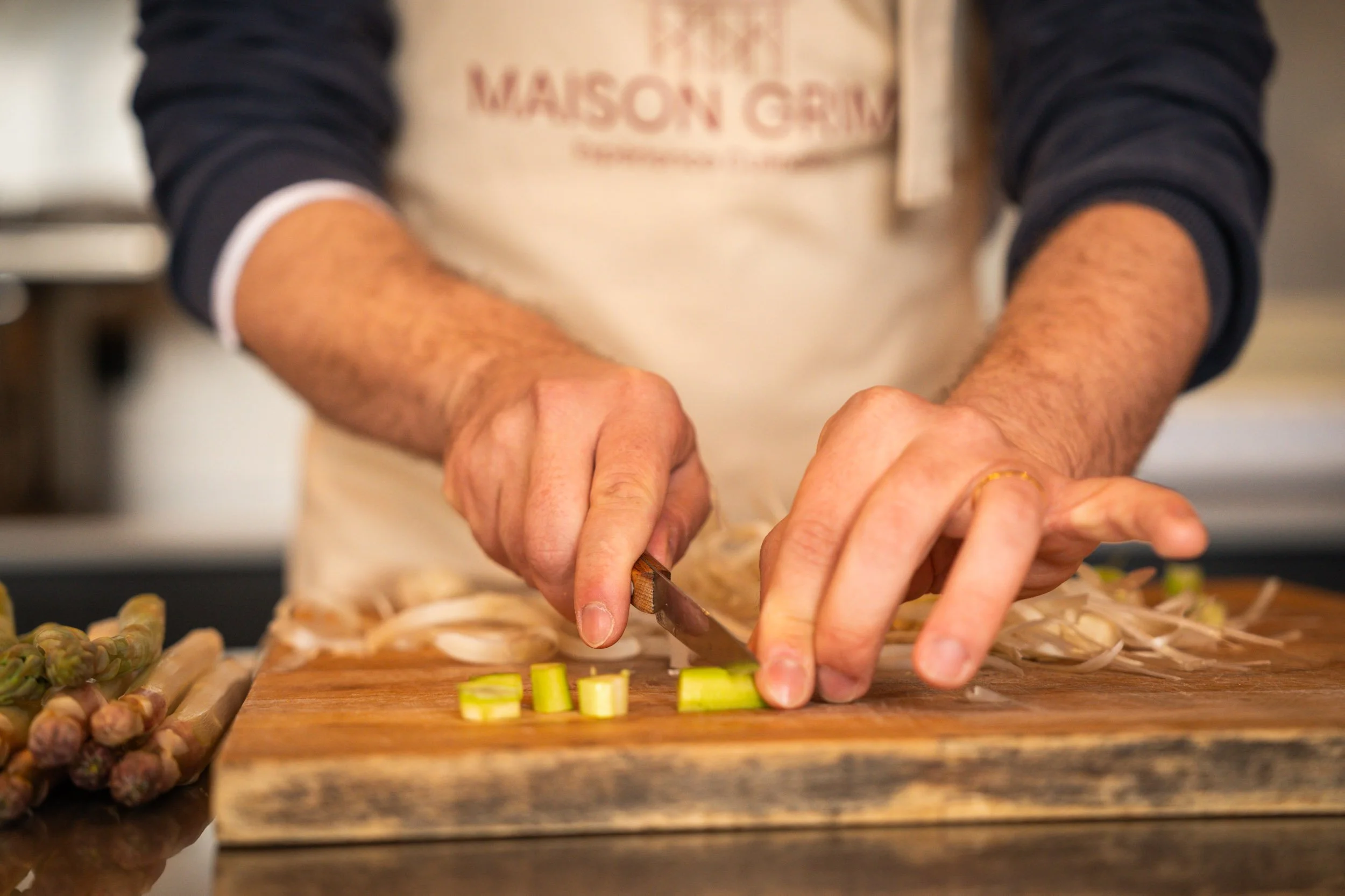 Personne coupant des morceaux de céleri sur une planche en bois, portant un tablier.