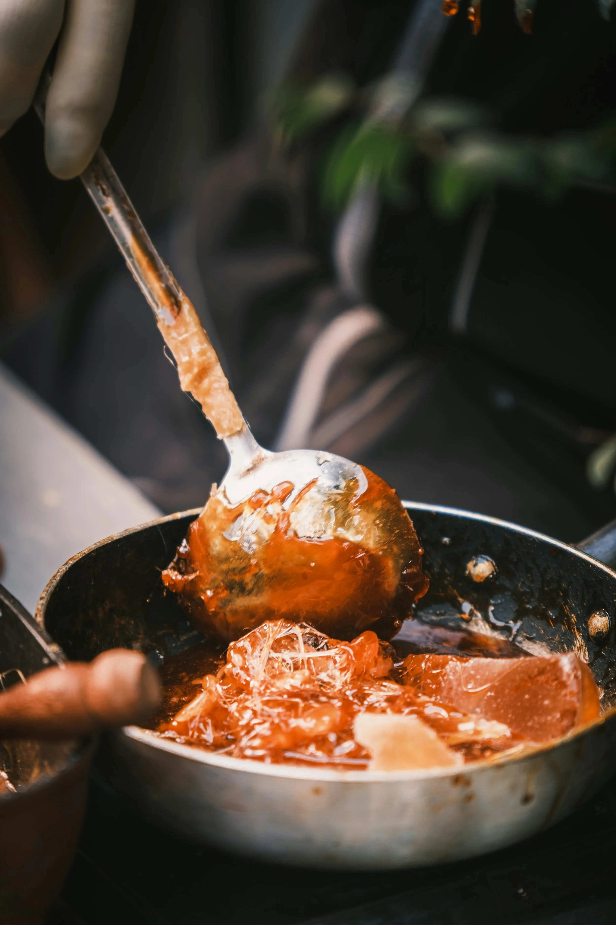 Cuillère en métal avec de la pâte à tartiner dans une poêle, fondue et filante, entourée d'un liquide brunâtre.